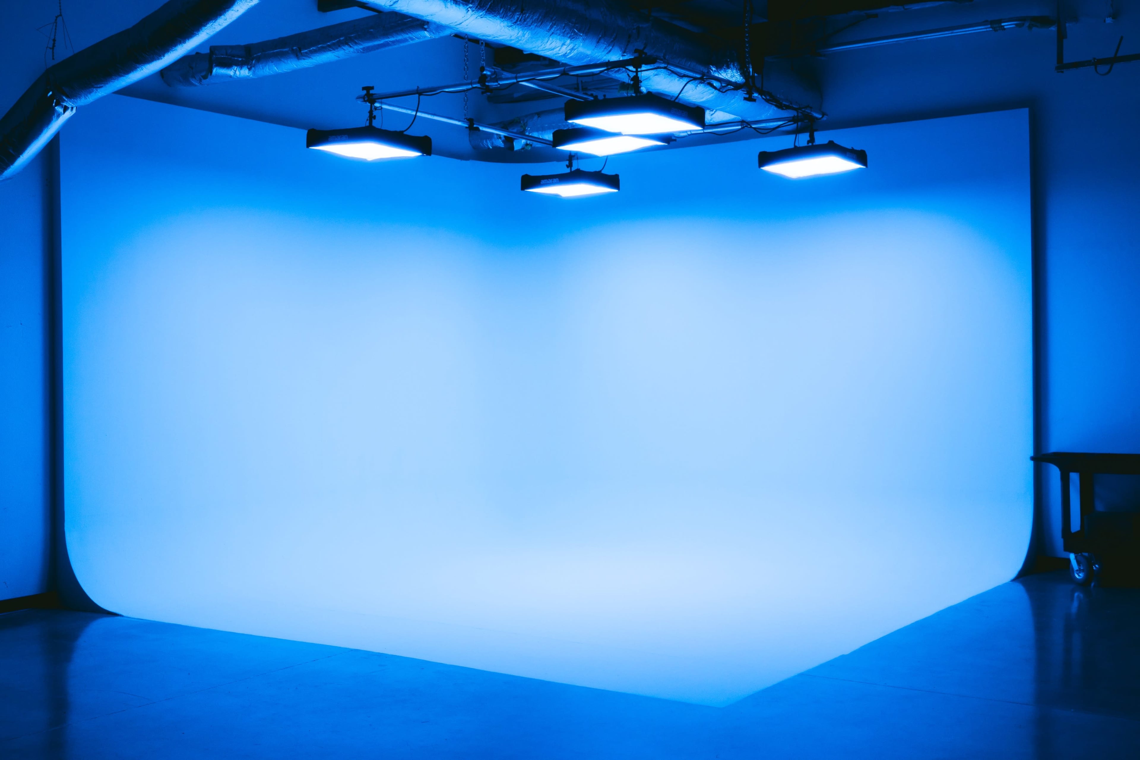 A photography studio with a blue backdrop and overhead lights illuminating the scene.