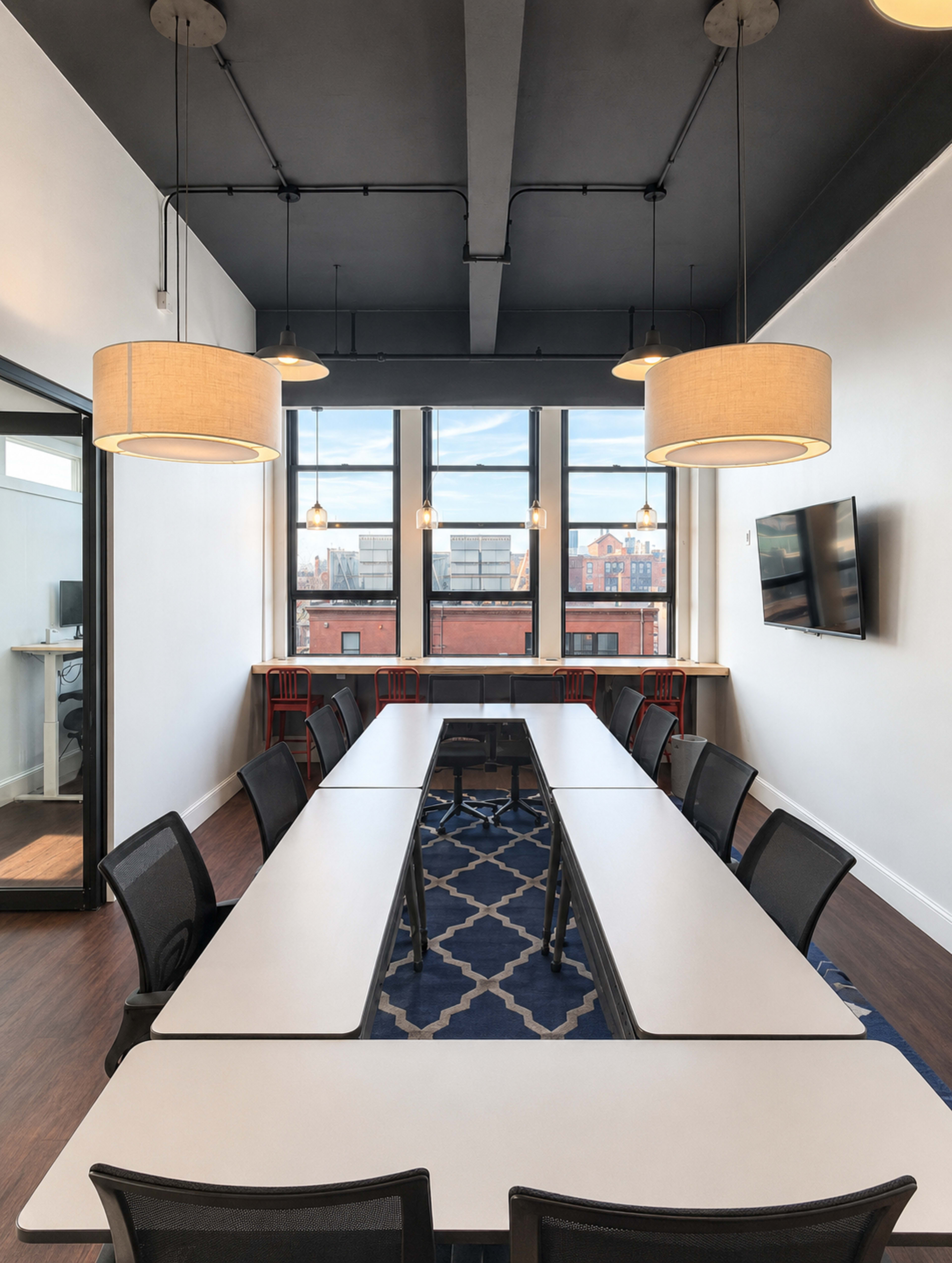 The image shows a modern conference room with a long table, chairs, and large windows allowing natural light to enter.