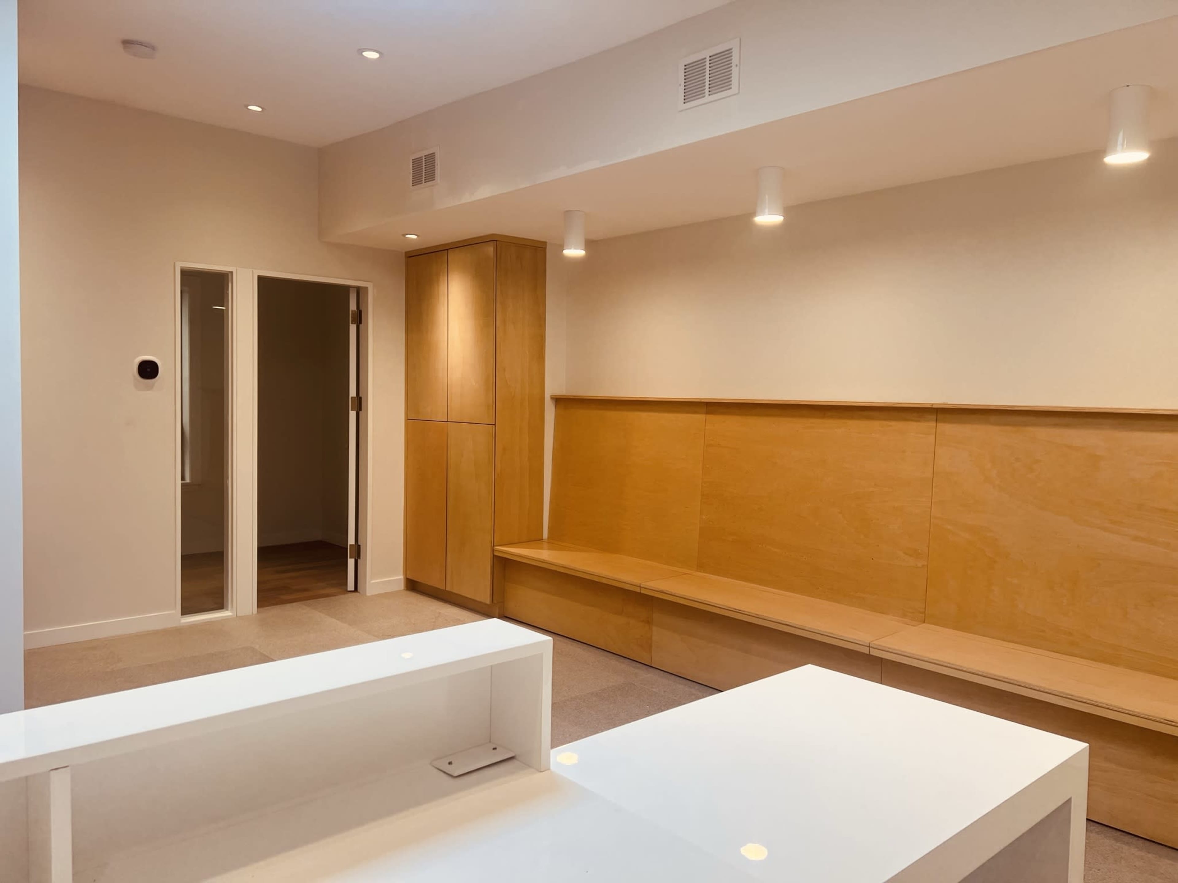 A minimalistic interior space featuring wooden paneling, a white counter, and walls equipped with recessed lighting.