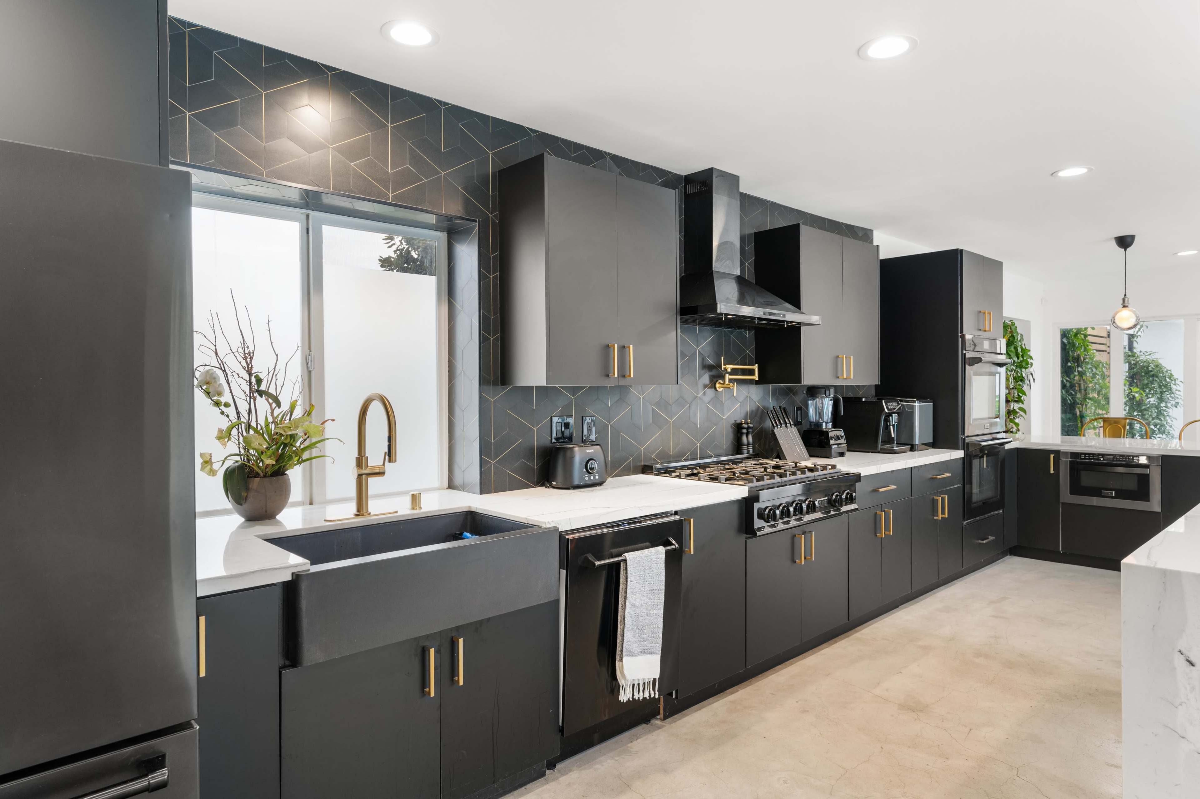 The modern kitchen features sleek black cabinetry, a stainless steel range hood, and a white countertop with a large sink facing a window.
