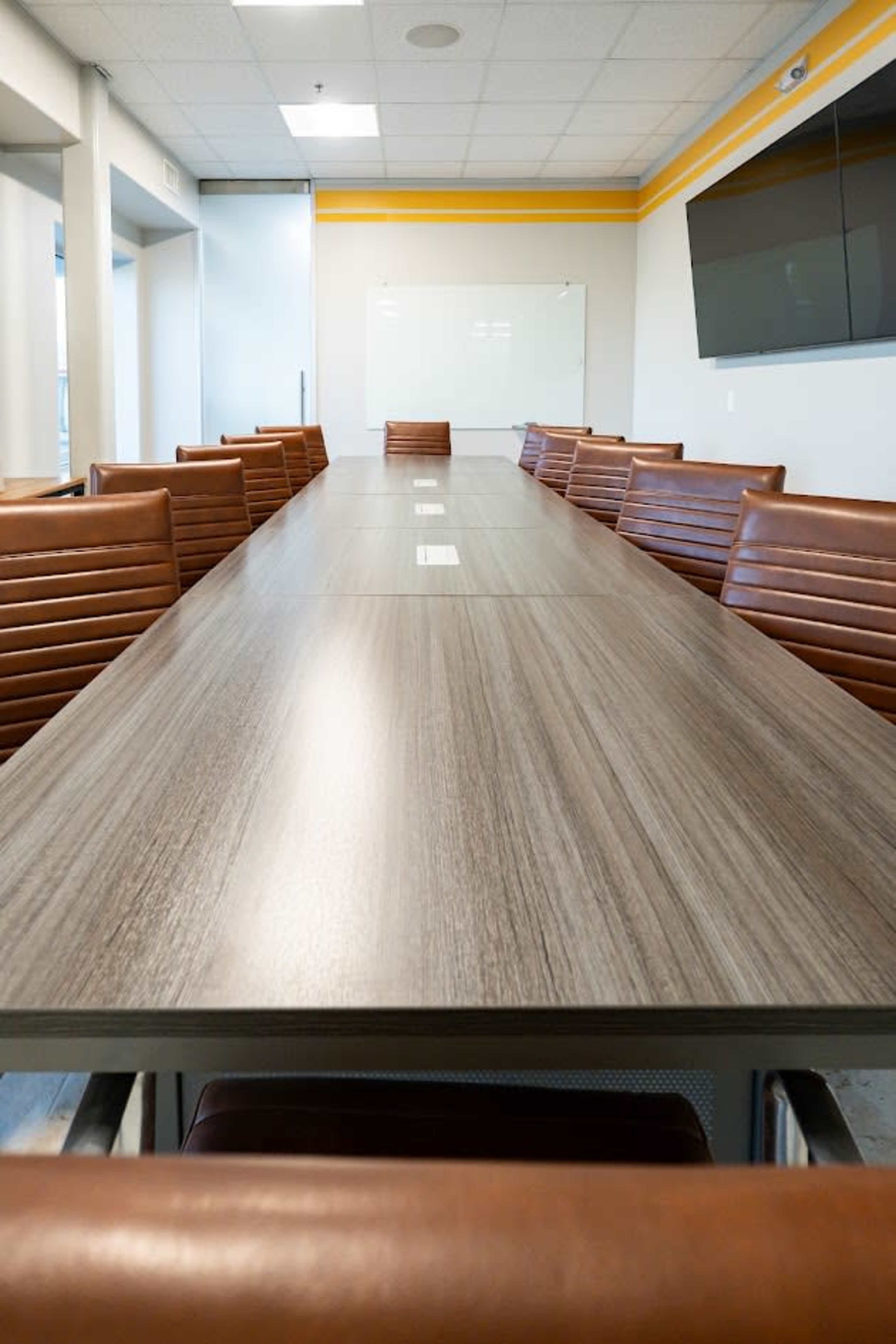 The image shows a long conference table surrounded by leather chairs in a brightly lit meeting room.