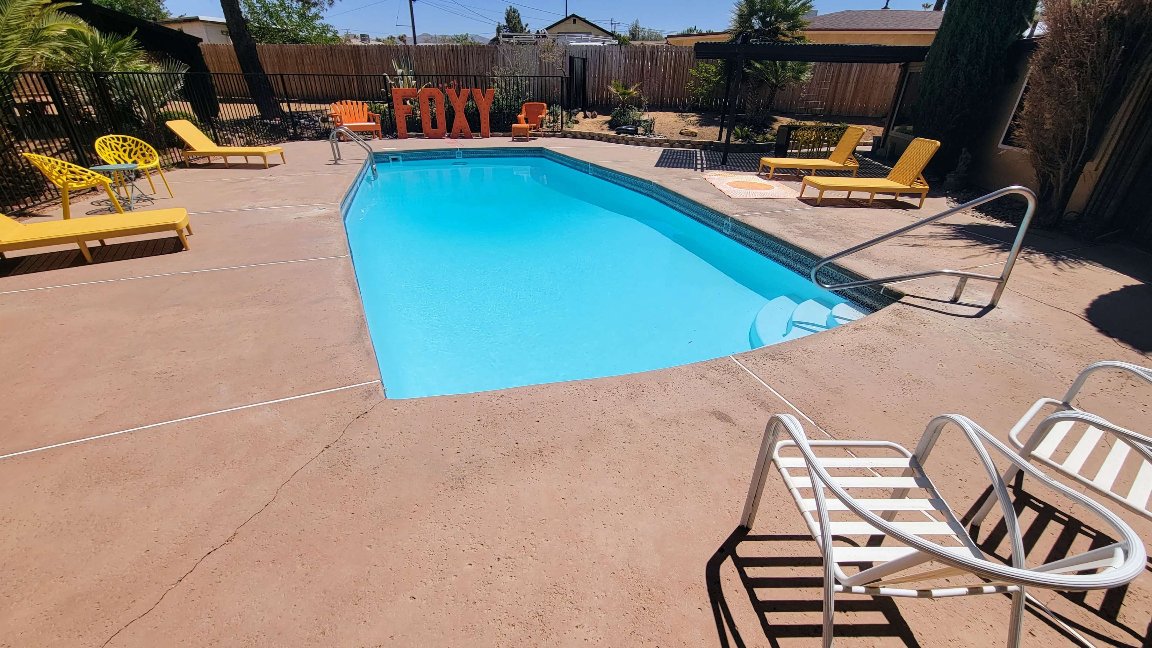 A clear swimming pool is surrounded by yellow lounge chairs and a large orange sign that reads "FOXY."