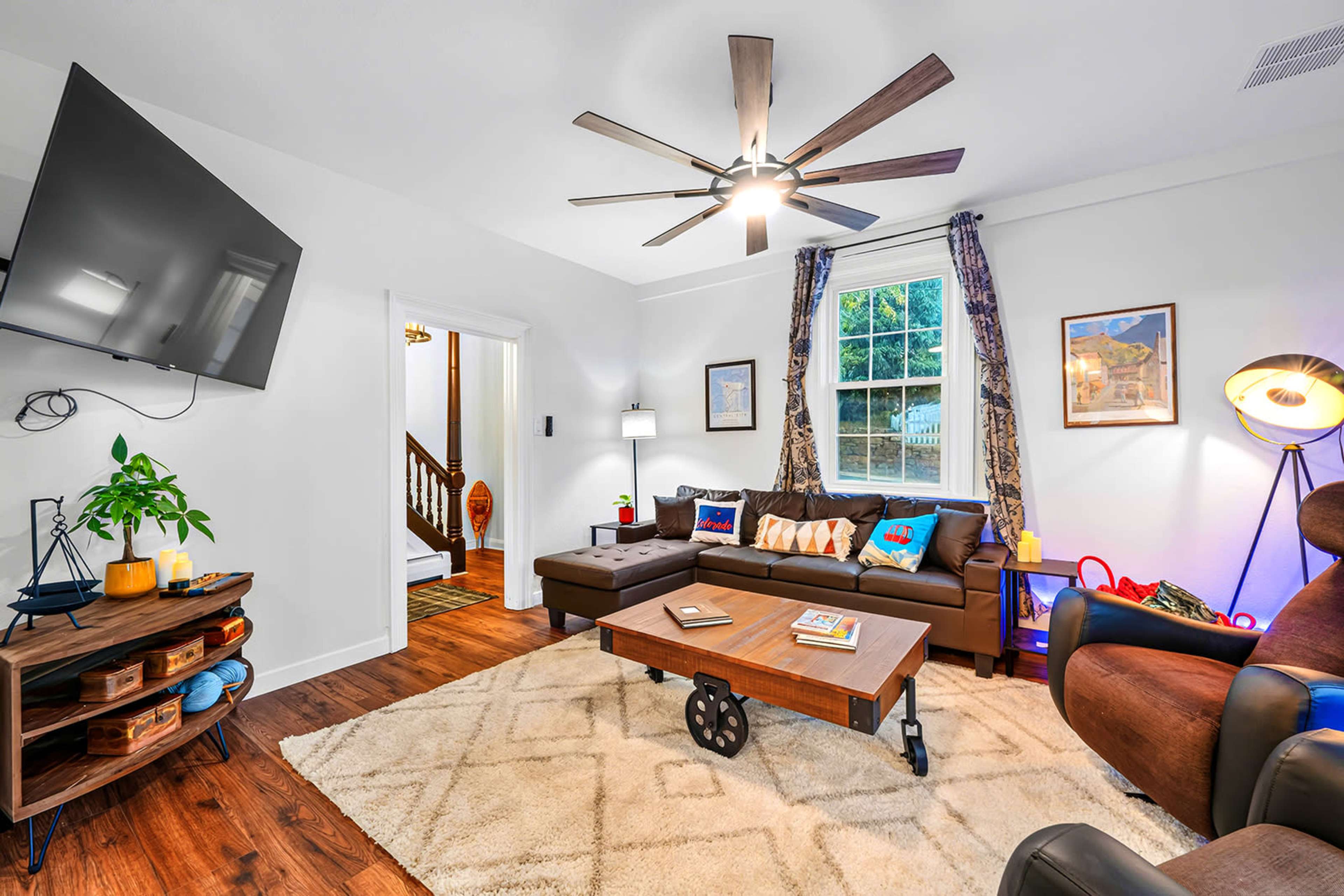 The living room features a large sectional sofa, a coffee table, and a mounted television, with a staircase visible in the background.