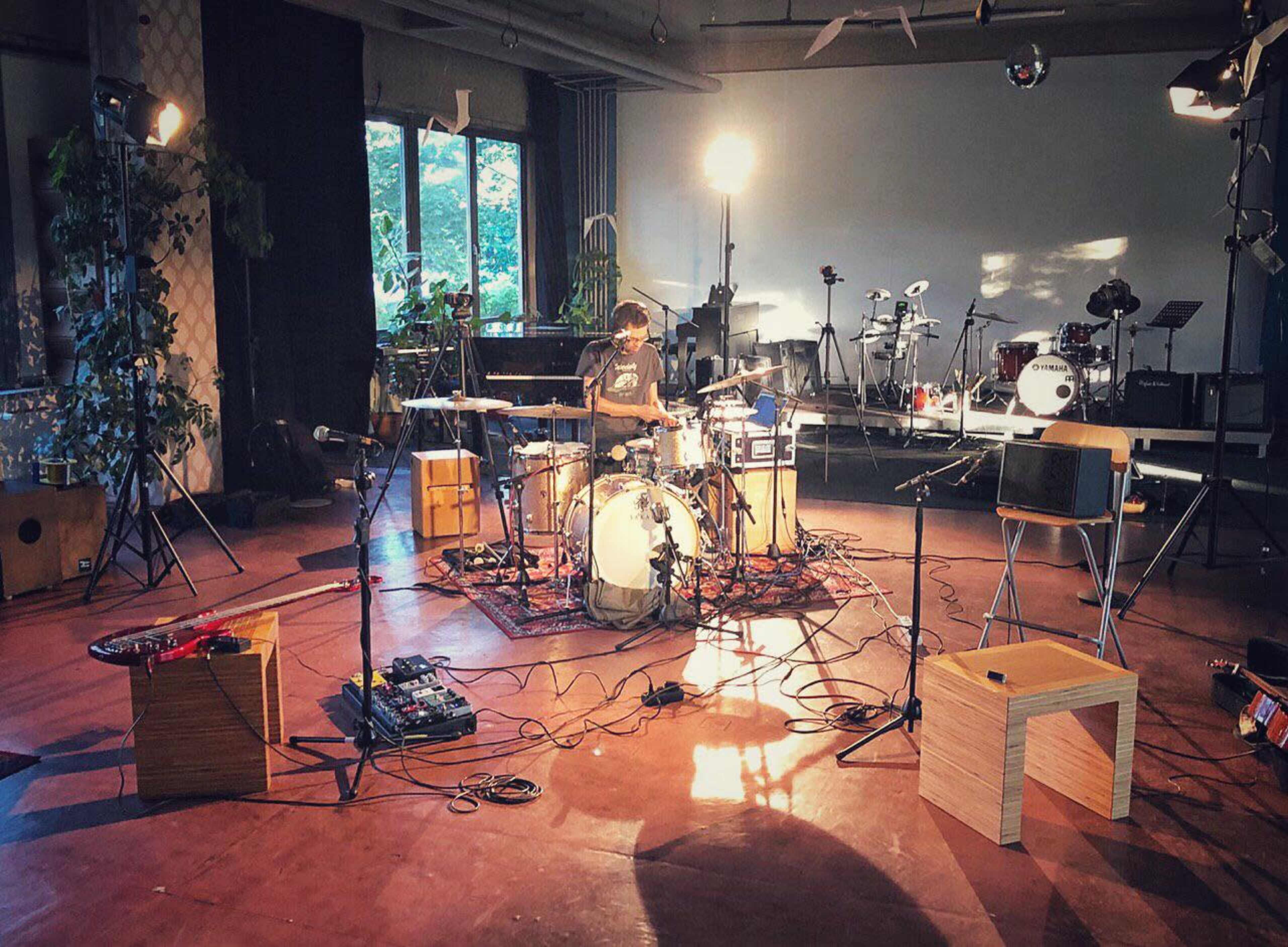 A musician playing drums in a spacious recording studio filled with various instruments and stage lighting.