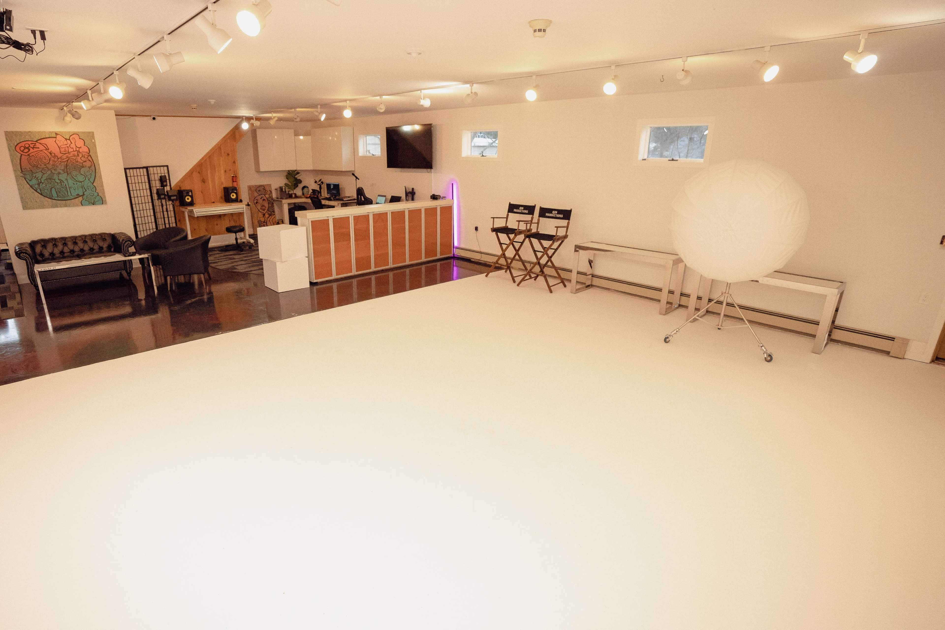 A spacious, brightly lit studio with a modern kitchenette, seating area, and a large white backdrop.