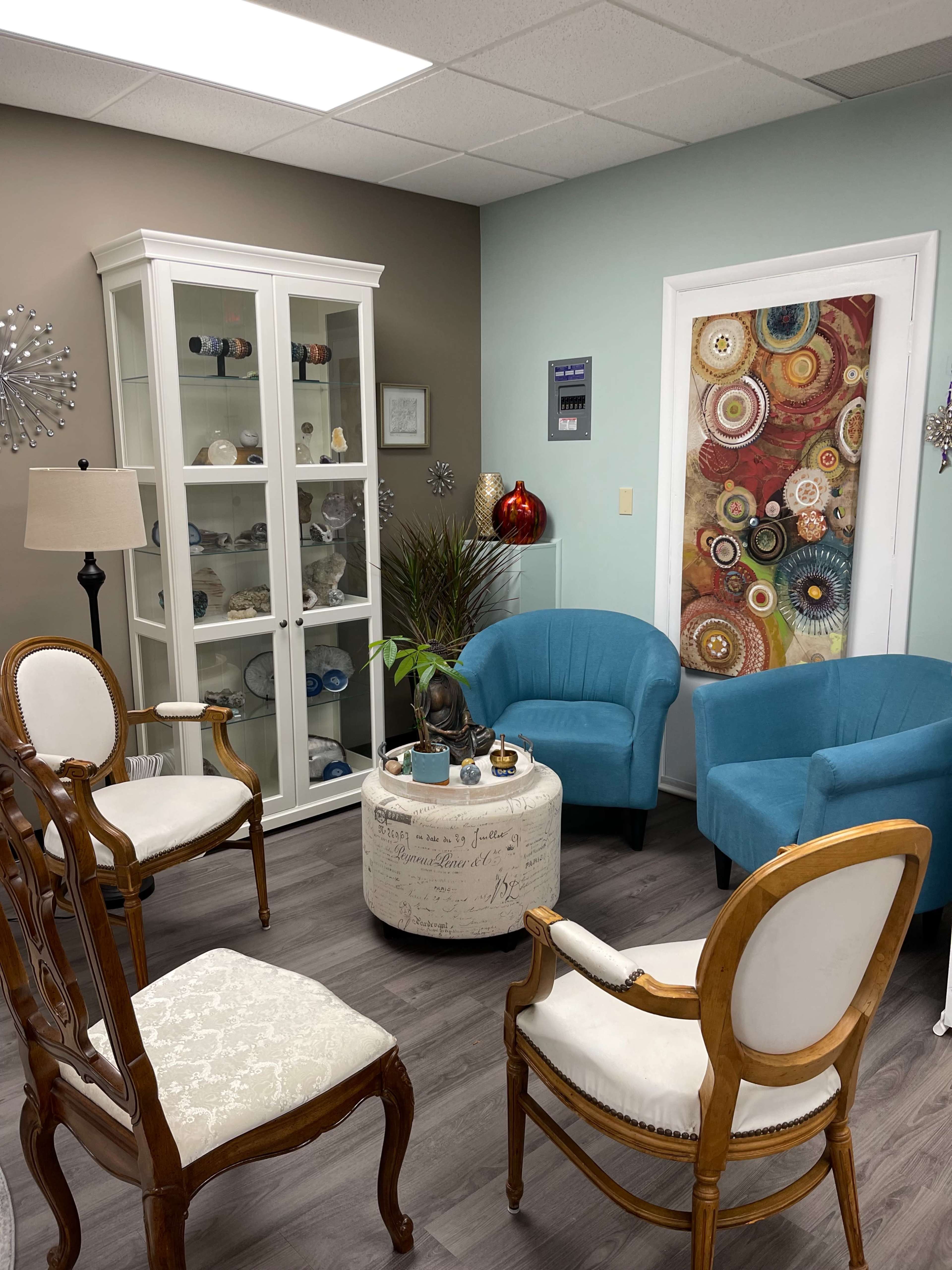 A cozy waiting room with four chairs, a glass display cabinet, and decorative wall art.
