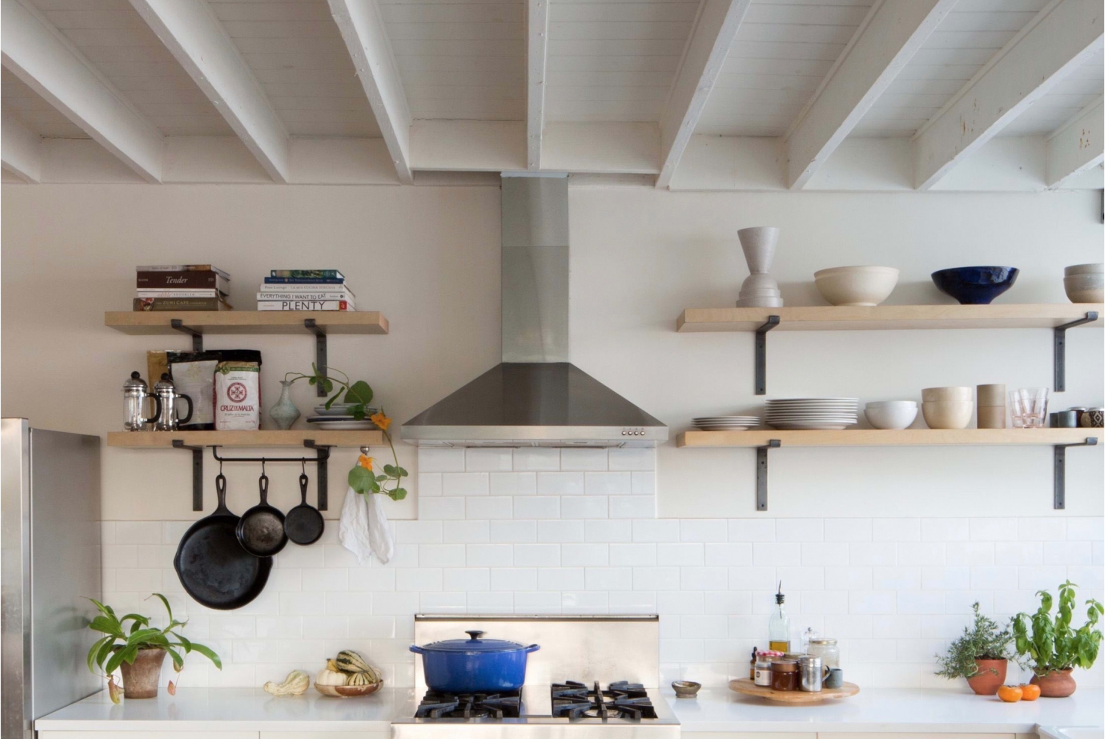 A modern kitchen featuring open shelves with various kitchenware, a stainless steel range hood, and a blue pot on the stove.