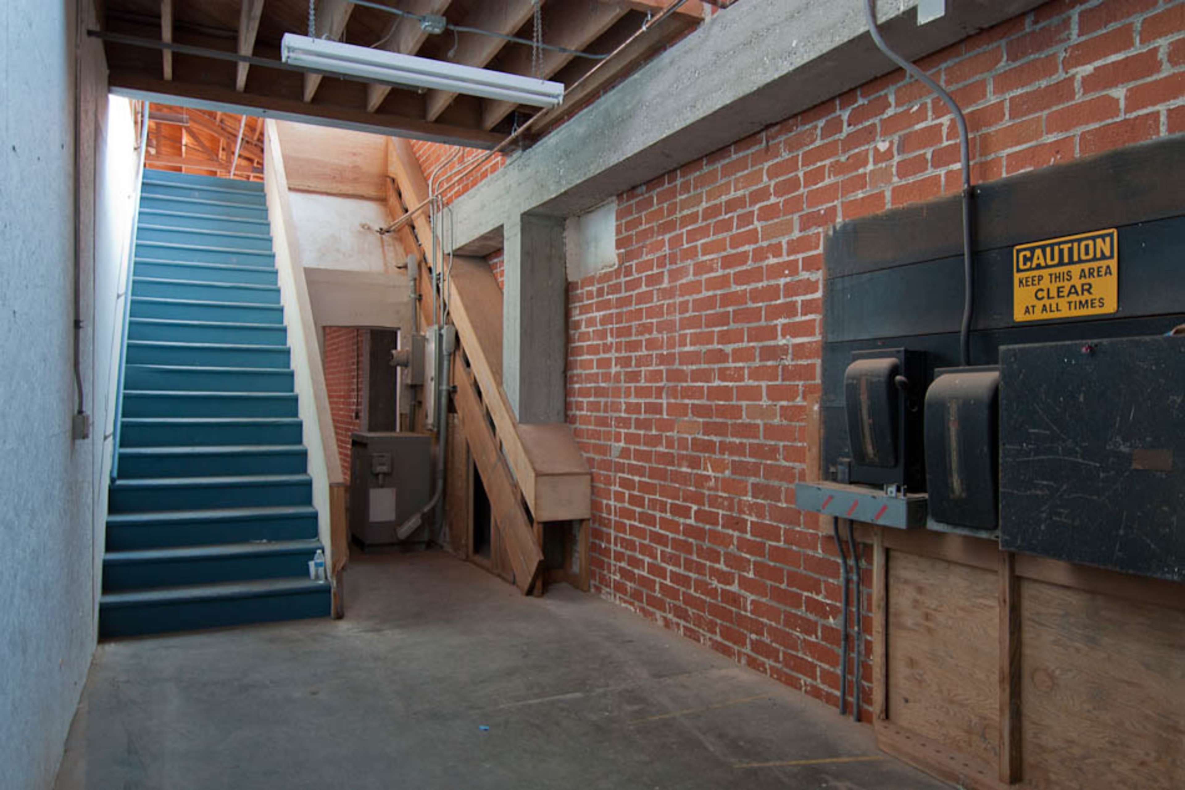 A bare interior space with exposed brick walls, a staircase leading to an upper level, and a warning sign on the wall.