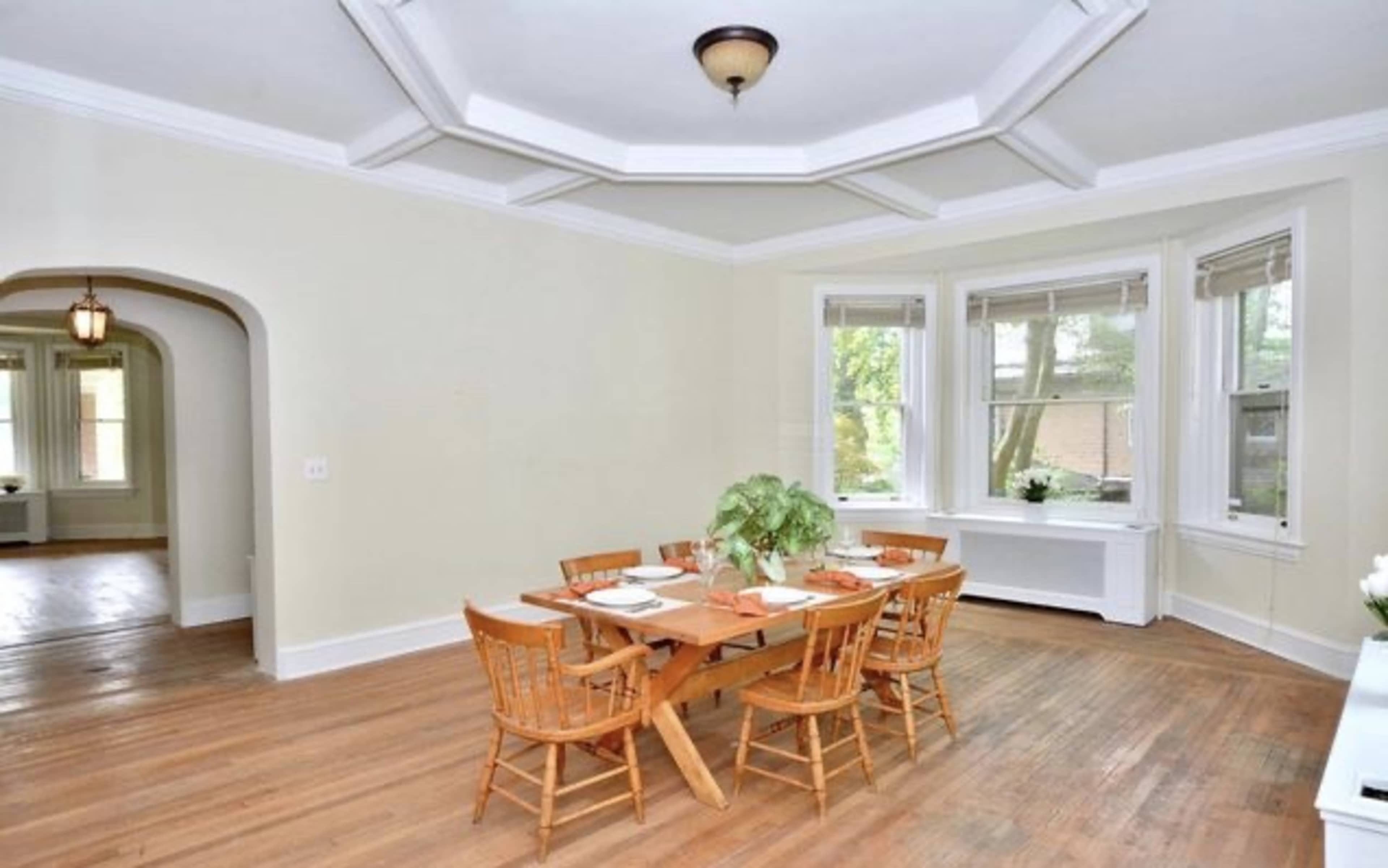 A wooden dining table is set for a meal in a room with large windows and a coffered ceiling.