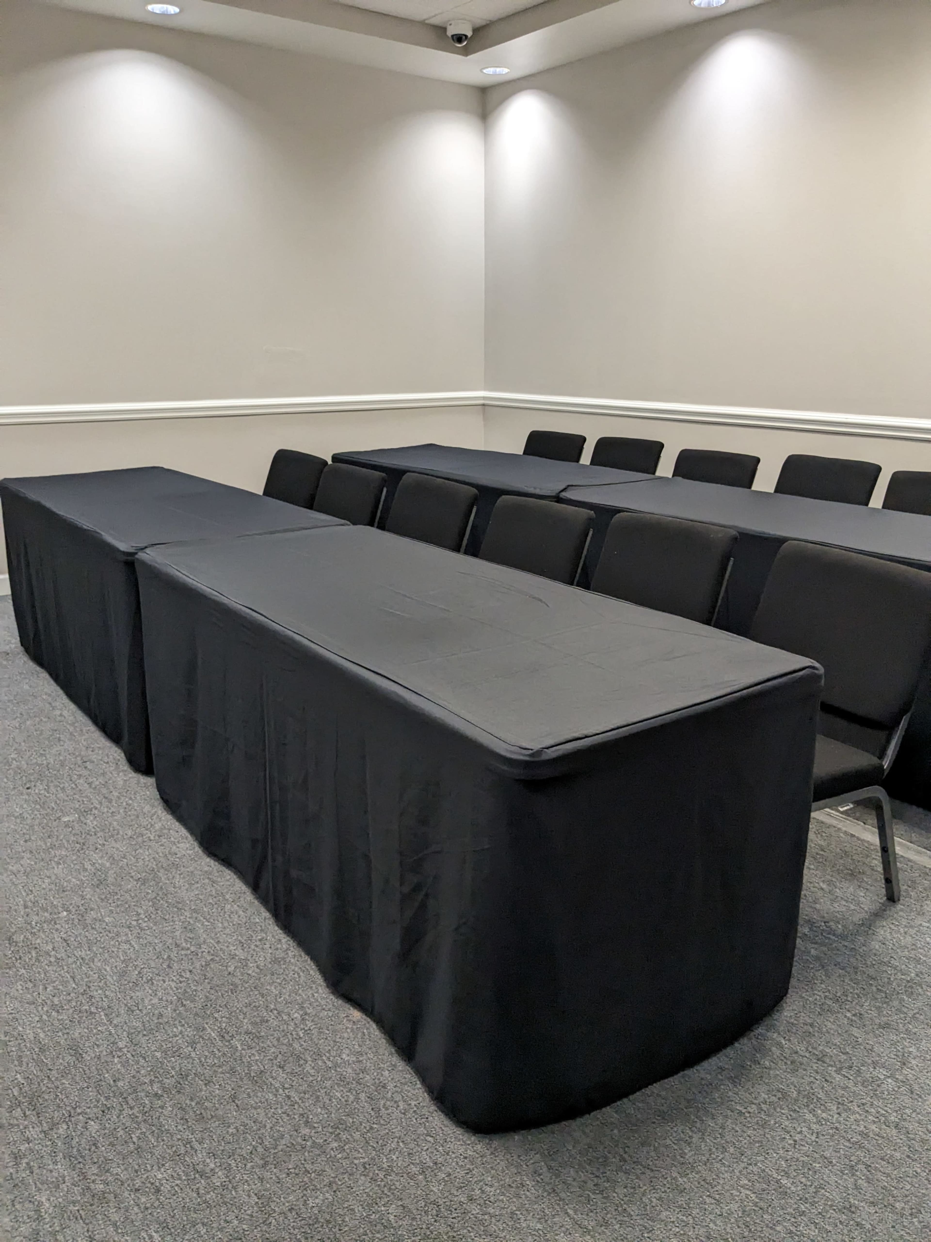 A small conference room with two long black tables covered with cloth and several black chairs arranged behind them.