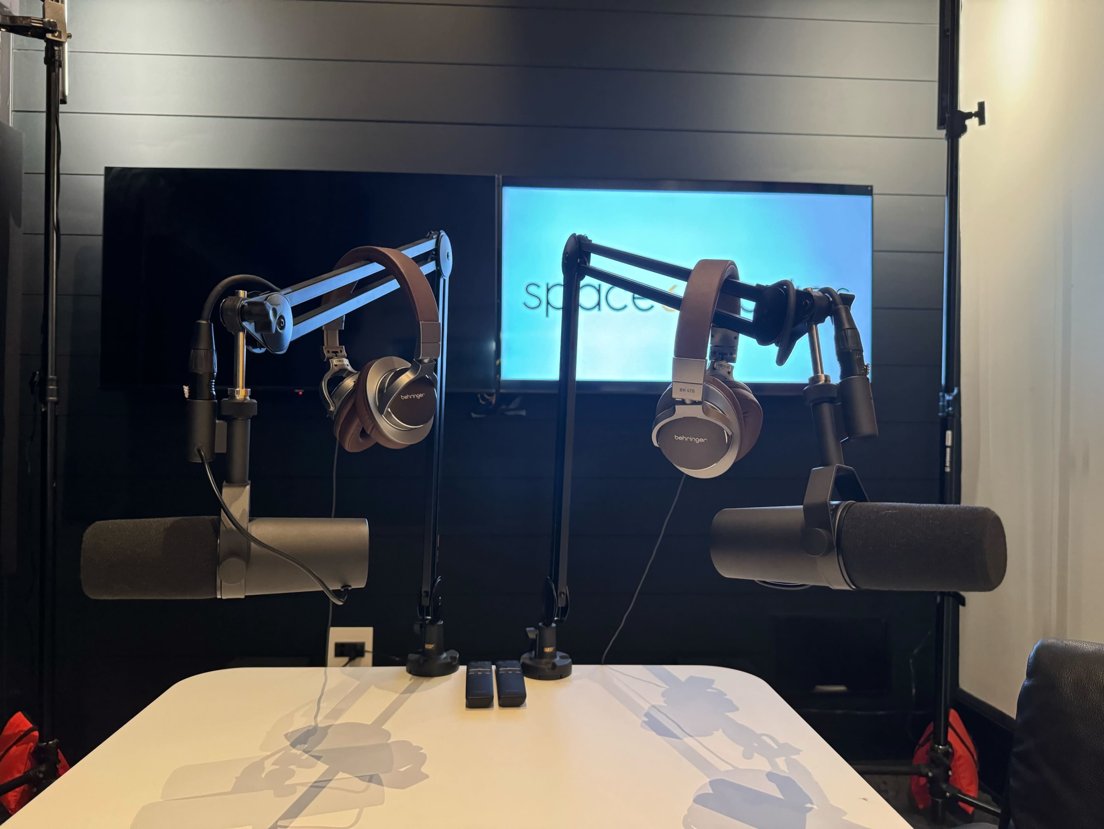 A podcast recording setup featuring two microphones and headphones mounted on adjustable arms, with a screen displaying the word "space" in the background.
