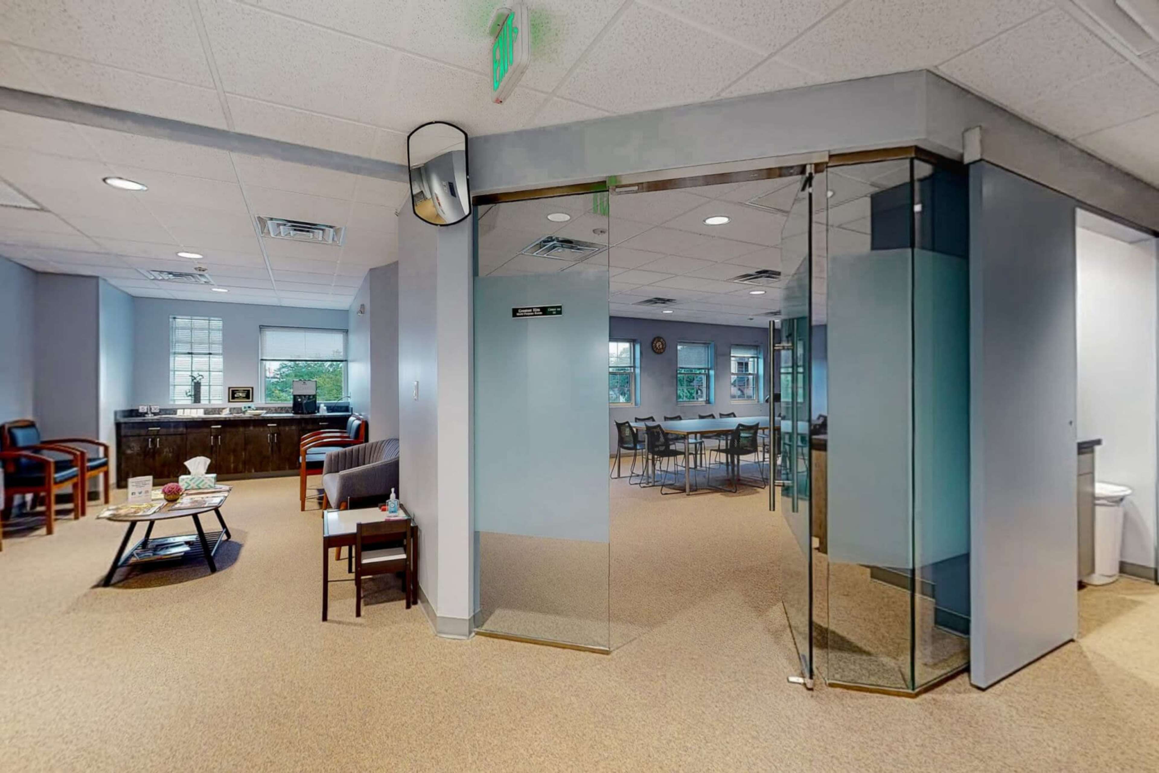 A modern office space with glass sliding doors and seating areas, featuring a mix of chairs and tables in the background.