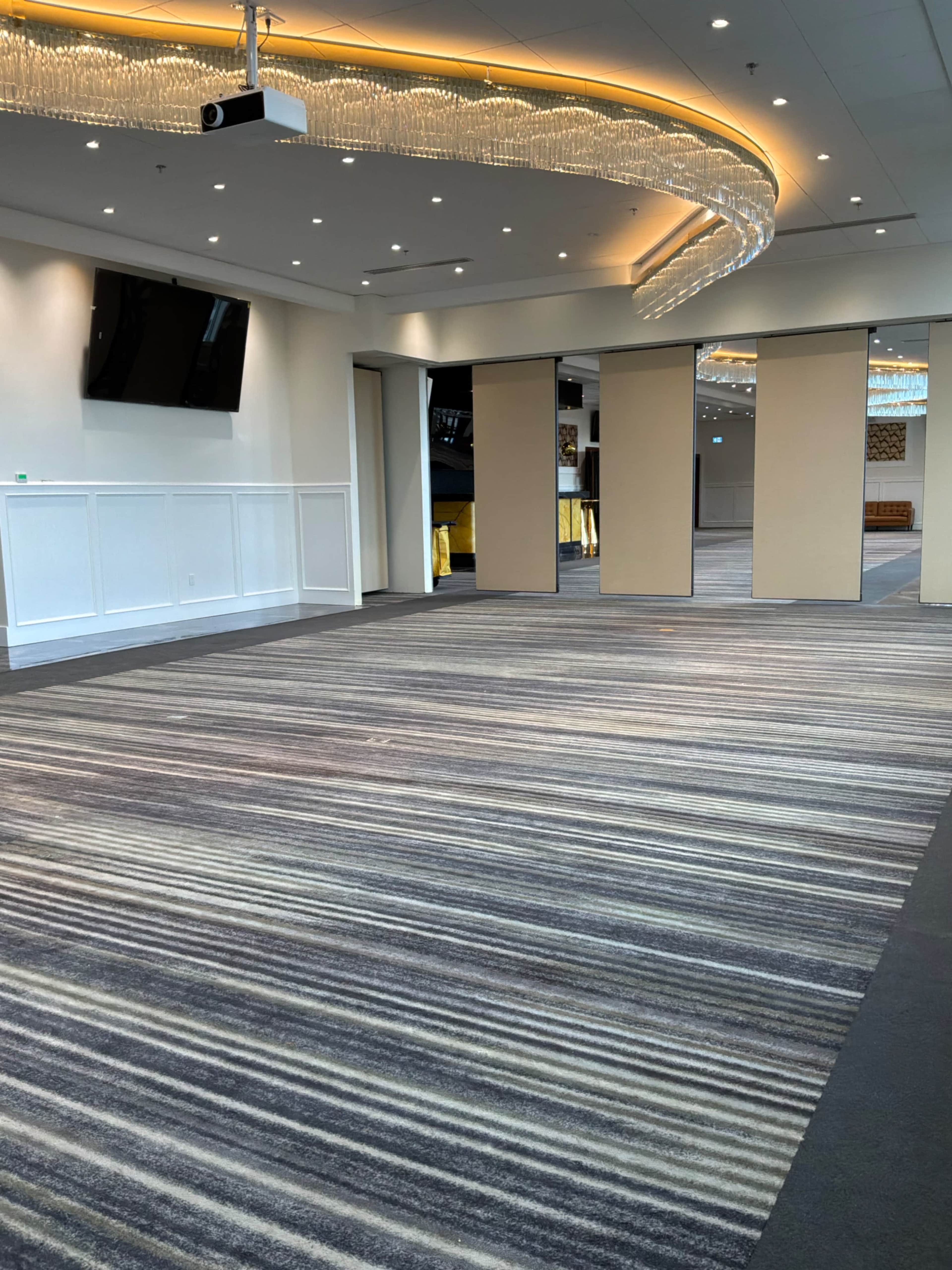 The image shows an empty room with a striped carpet, feature lighting, and large wall panels.