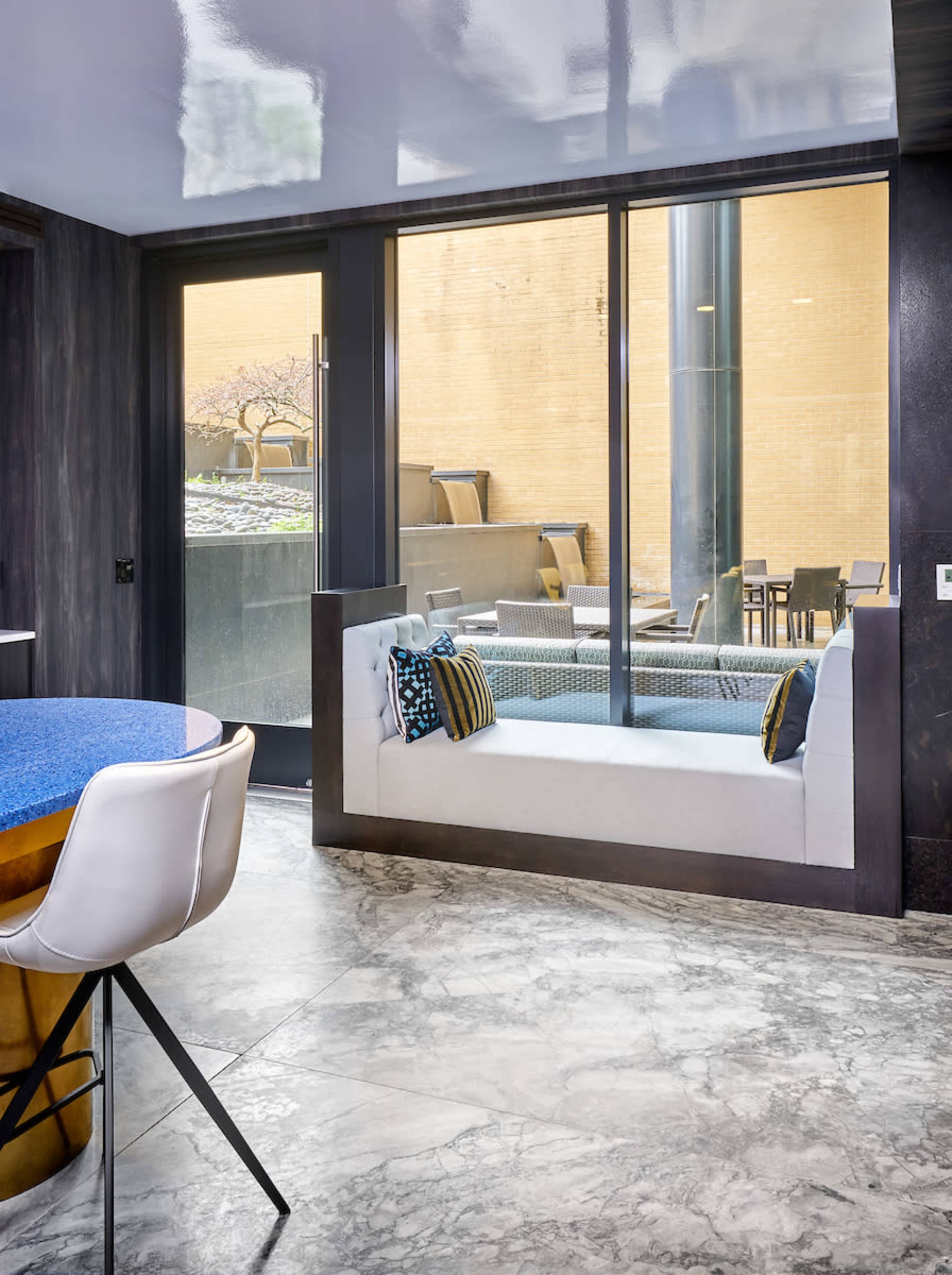 A modern lounge area features a window seat with patterned cushions overlooking an outdoor space with tables and chairs.