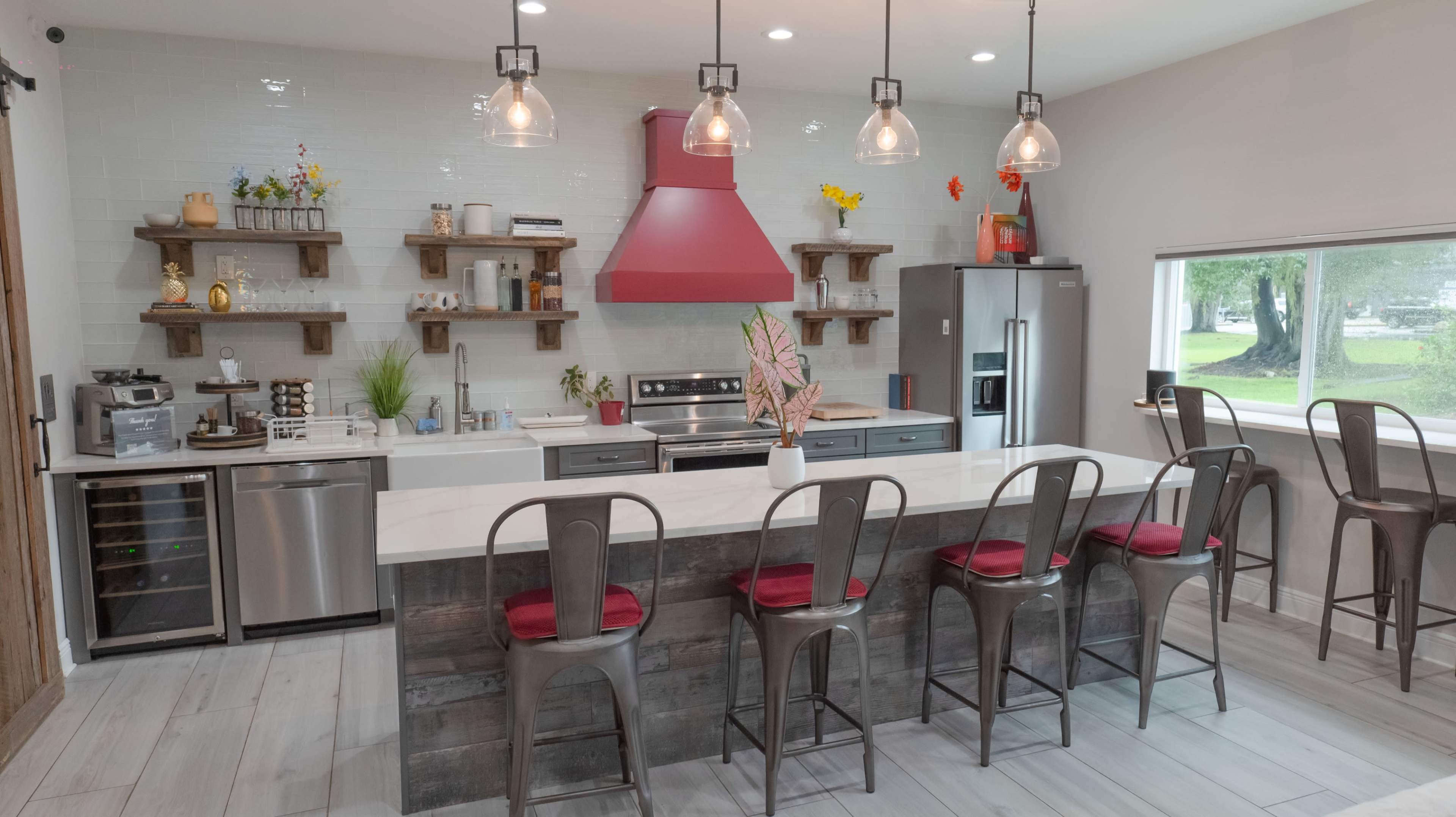 A modern kitchen features a central island with bar seating, stainless steel appliances, and a red range hood above the stove.