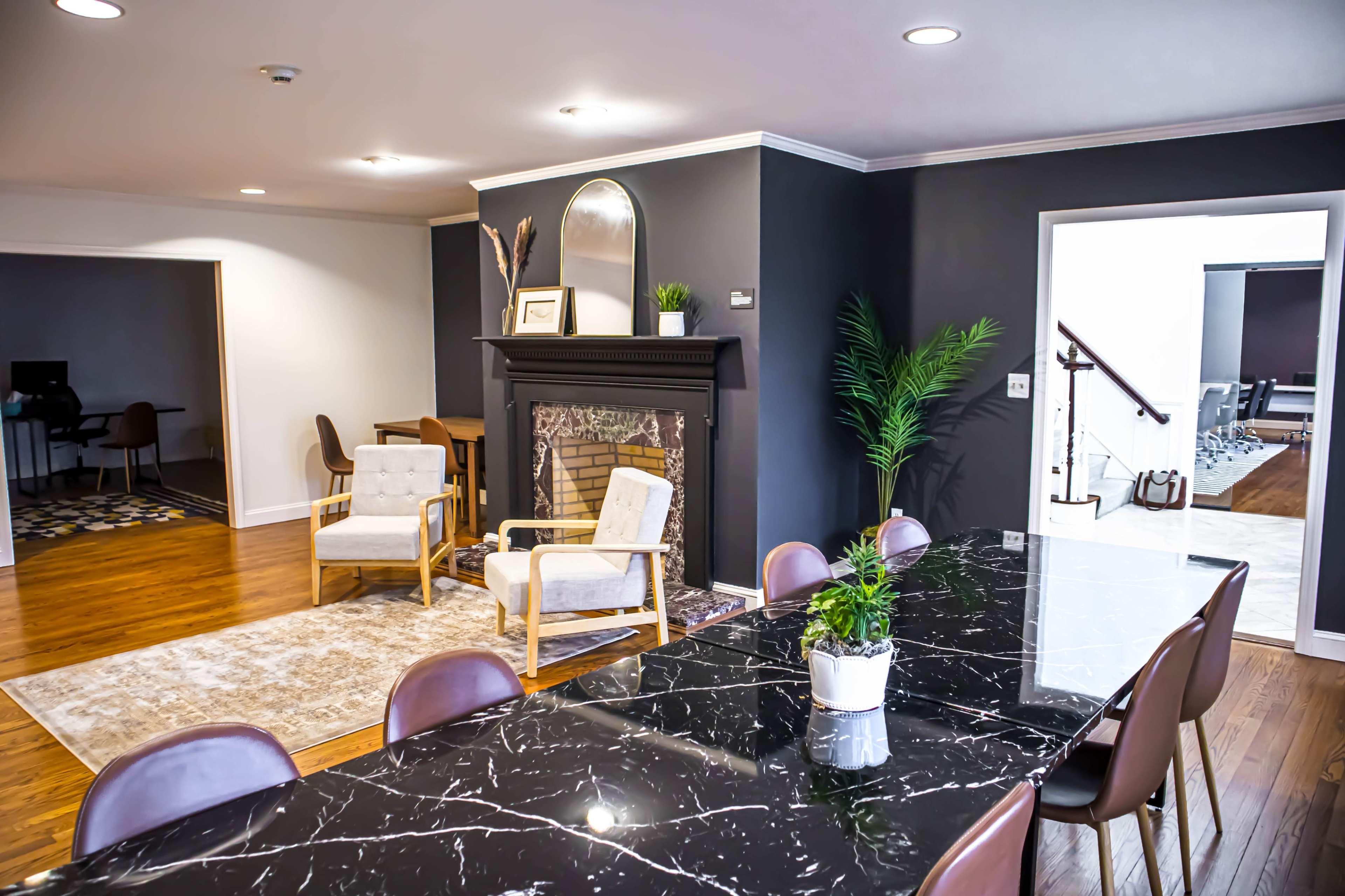 A modern interior space featuring a dining area with a black marble table, brown chairs, and a cozy seating arrangement by a fireplace.