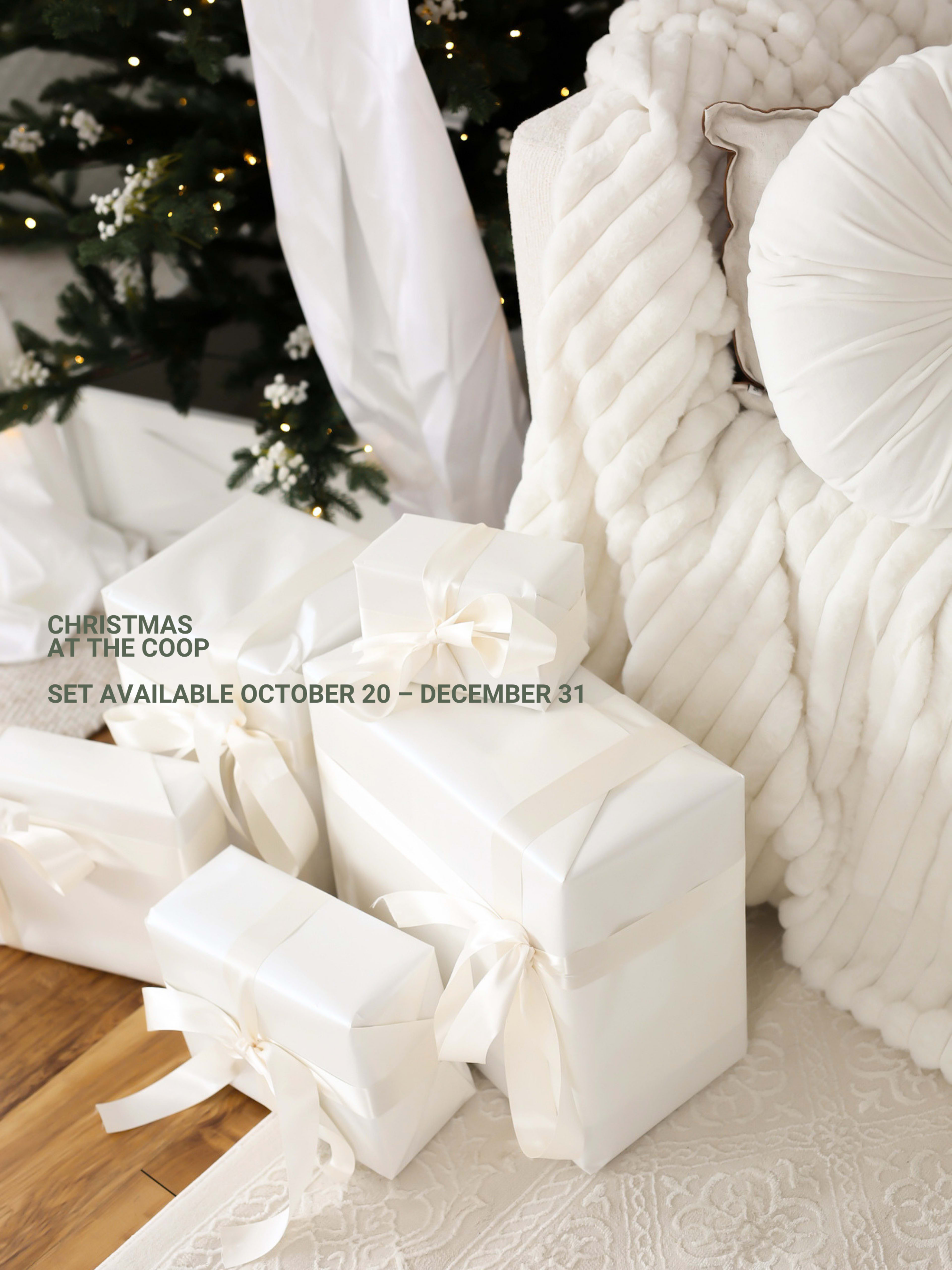 The image features several elegantly wrapped white gifts with bows arranged next to a cozy, textured throw blanket and a decorative pillow against a softly lit background, likely of a holiday setting.