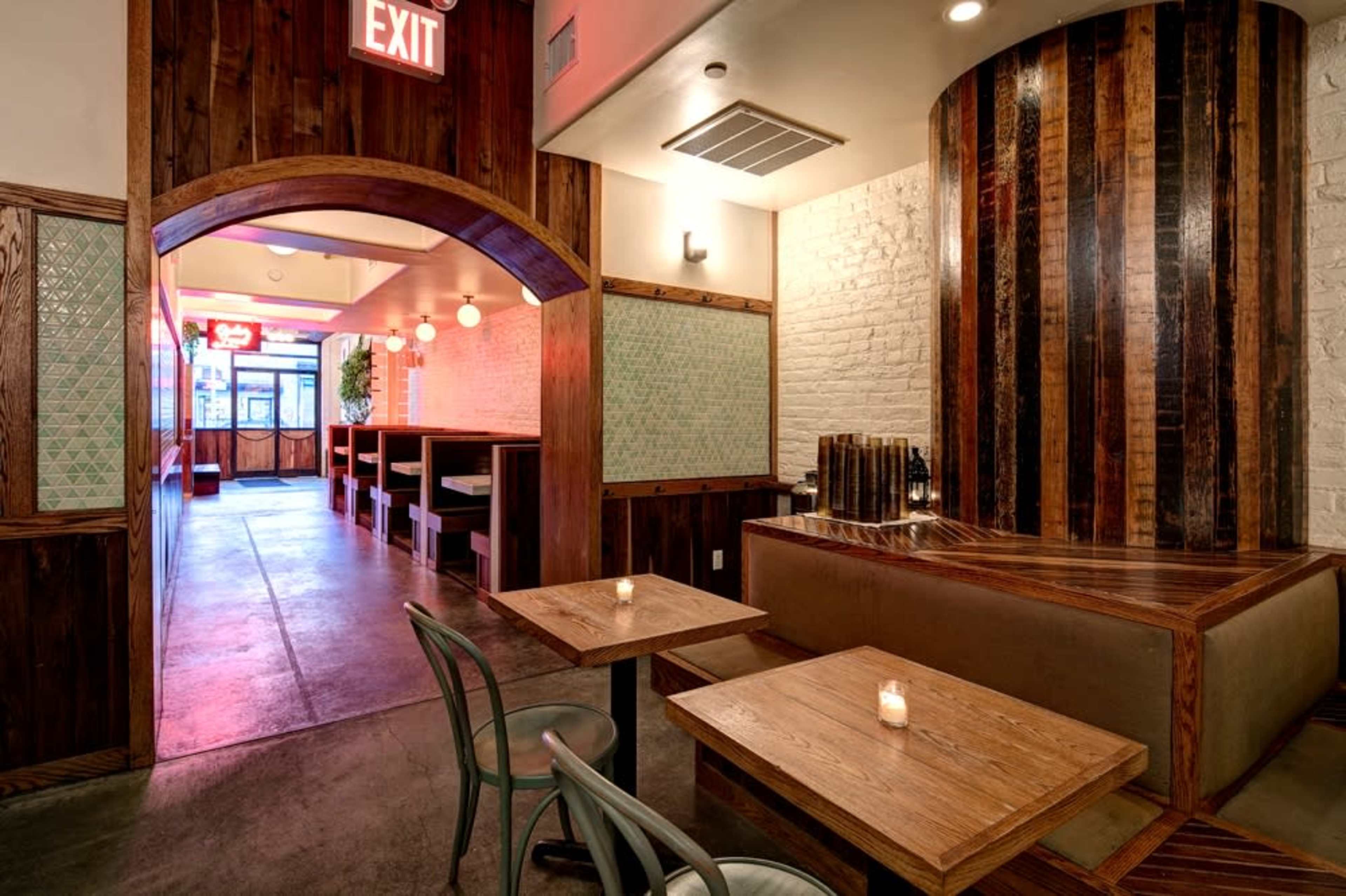 The image shows a modern restaurant interior featuring wooden accents, a cozy seating area with tables, and an exit sign illuminated in red.