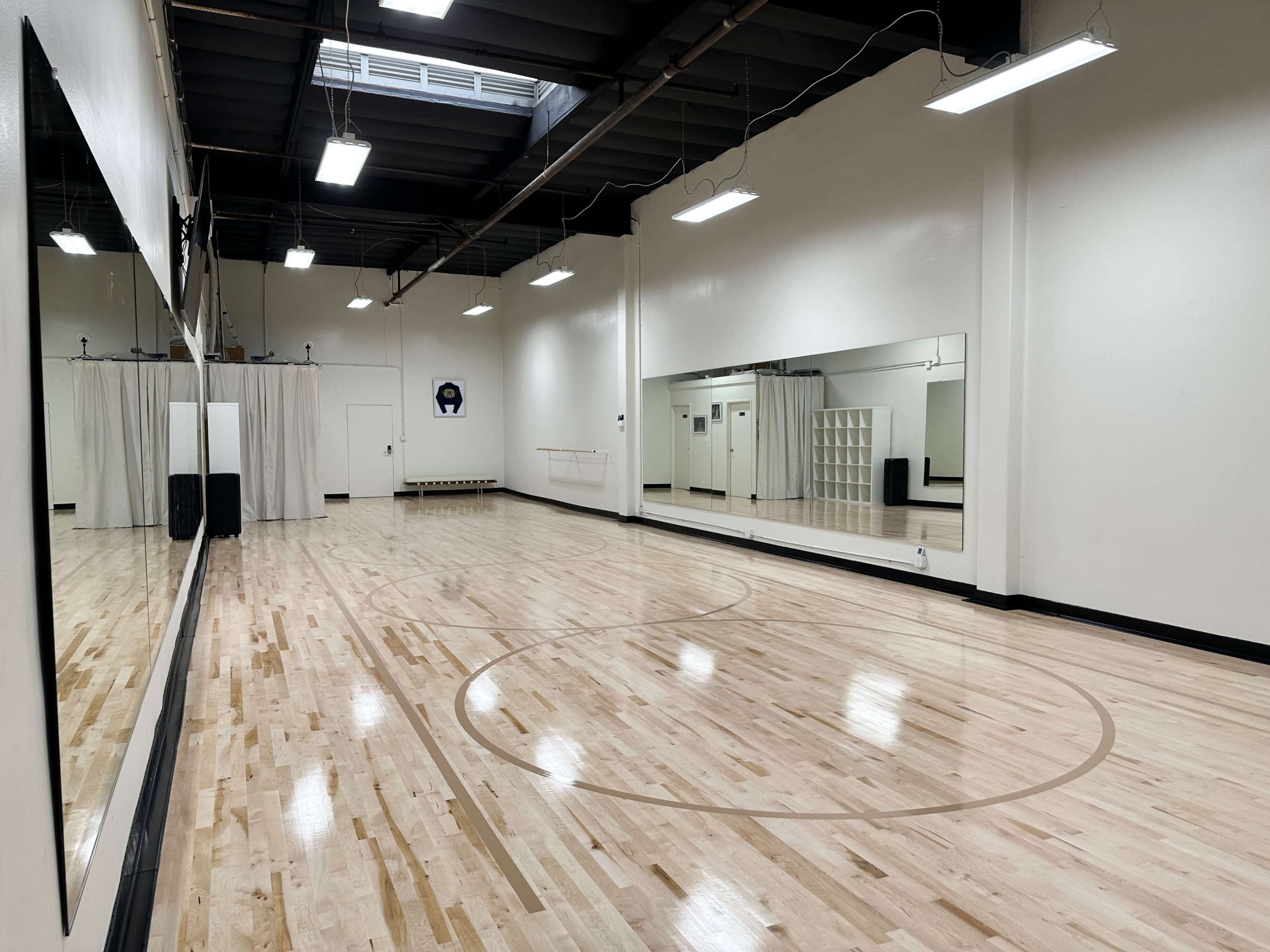 A spacious, empty dance studio with wooden flooring and large mirrors on one wall.