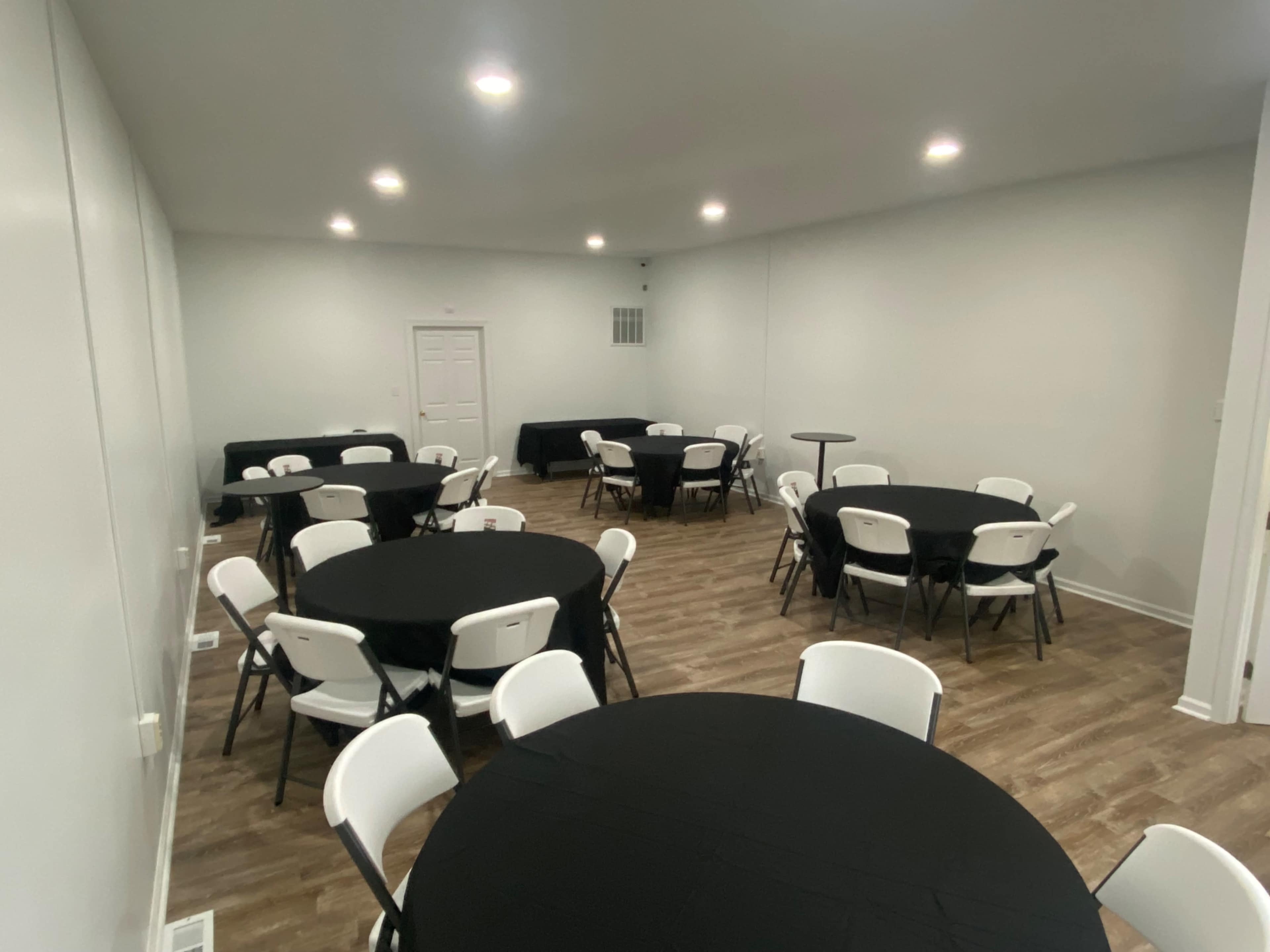 A meeting room with several round tables covered in black tablecloths and white chairs arranged throughout the space.