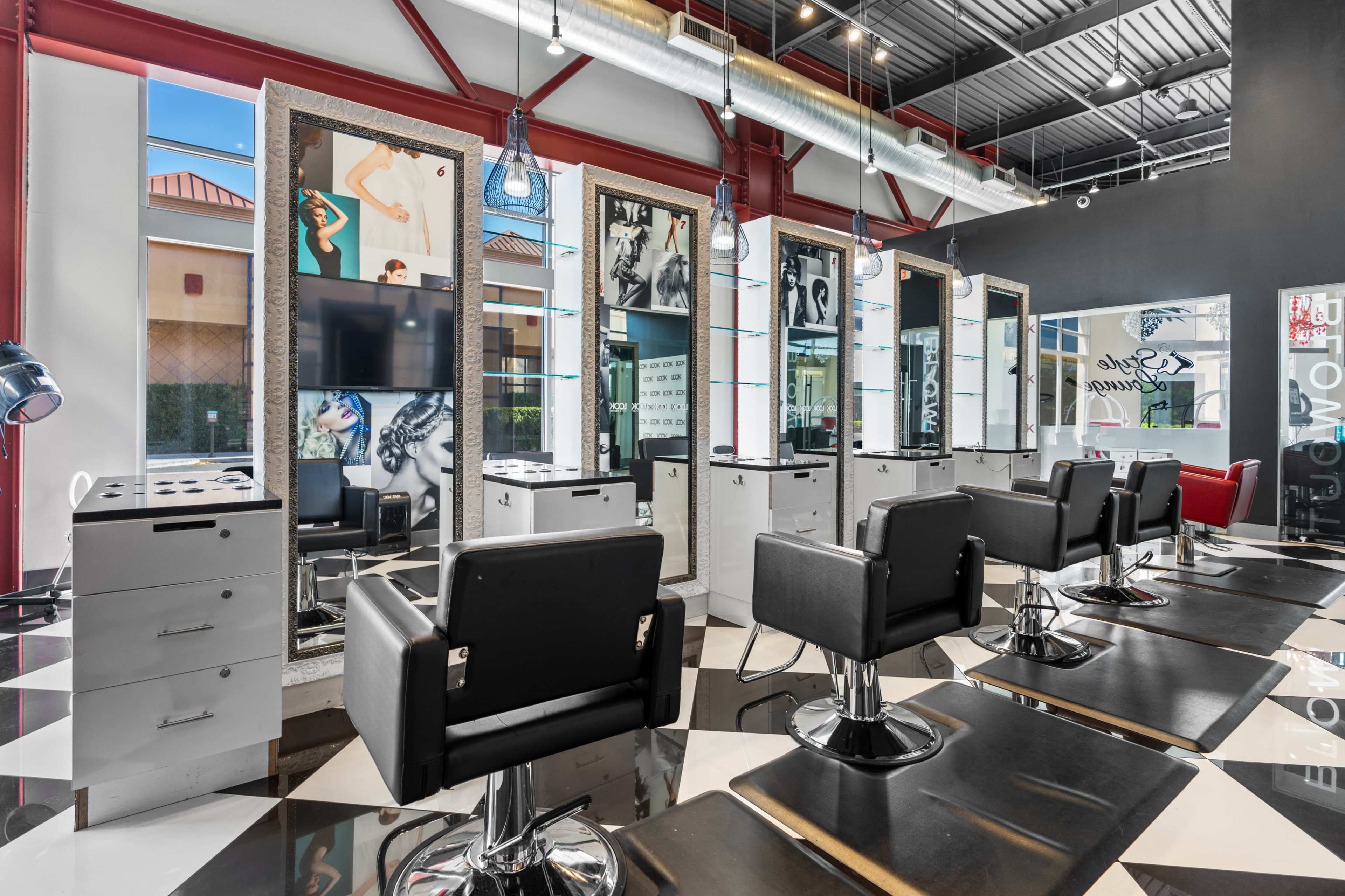A modern hair salon with black and white checkered flooring, featuring several styling stations equipped with chairs and mirrors.