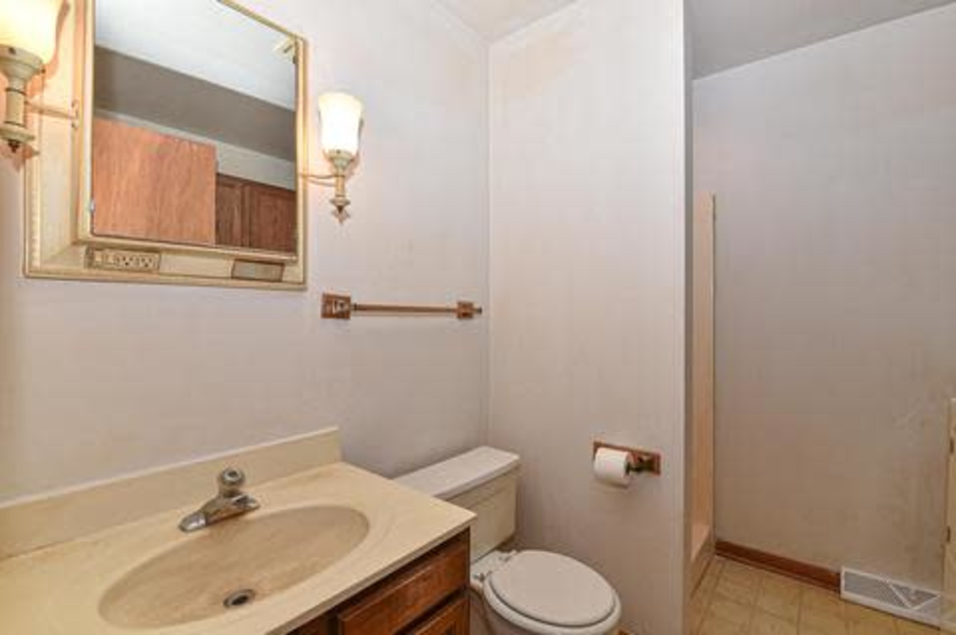 A small bathroom featuring a sink with a mirror above it, a toilet, and a separate shower area.