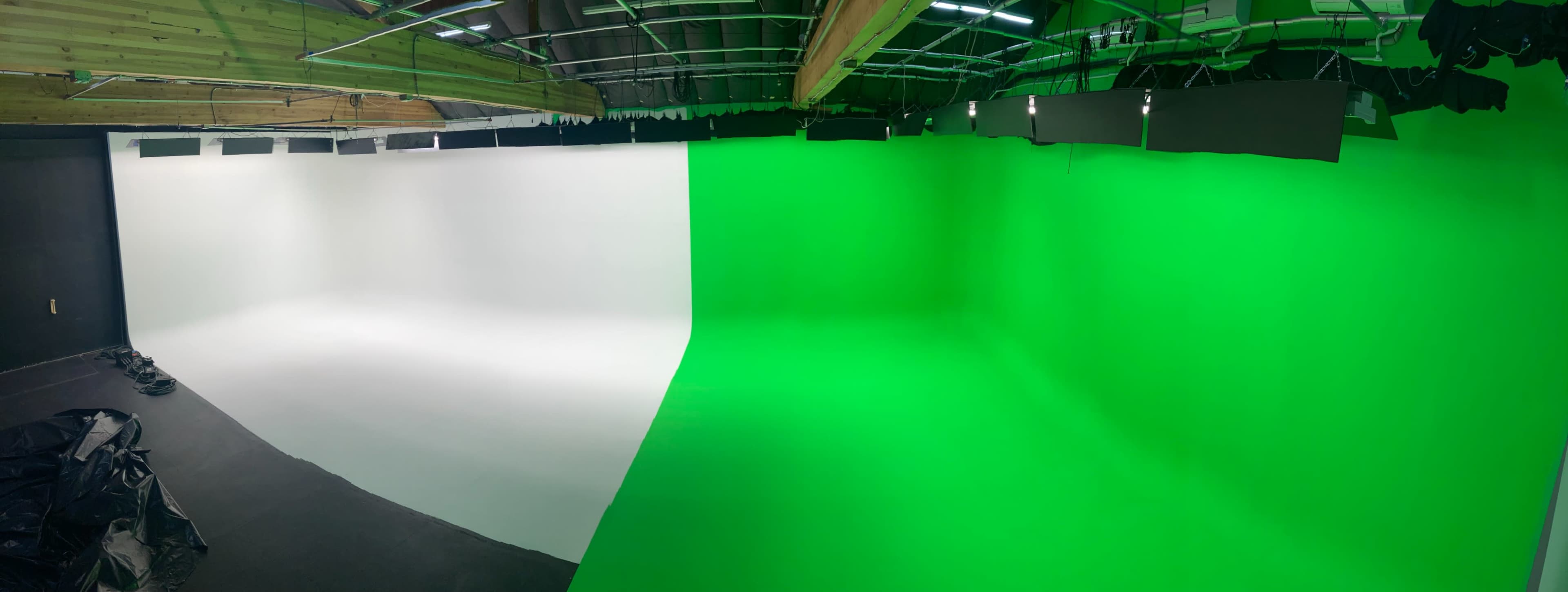 A panoramic view of a photography studio featuring a white backdrop on one side and a green screen backdrop on the other.