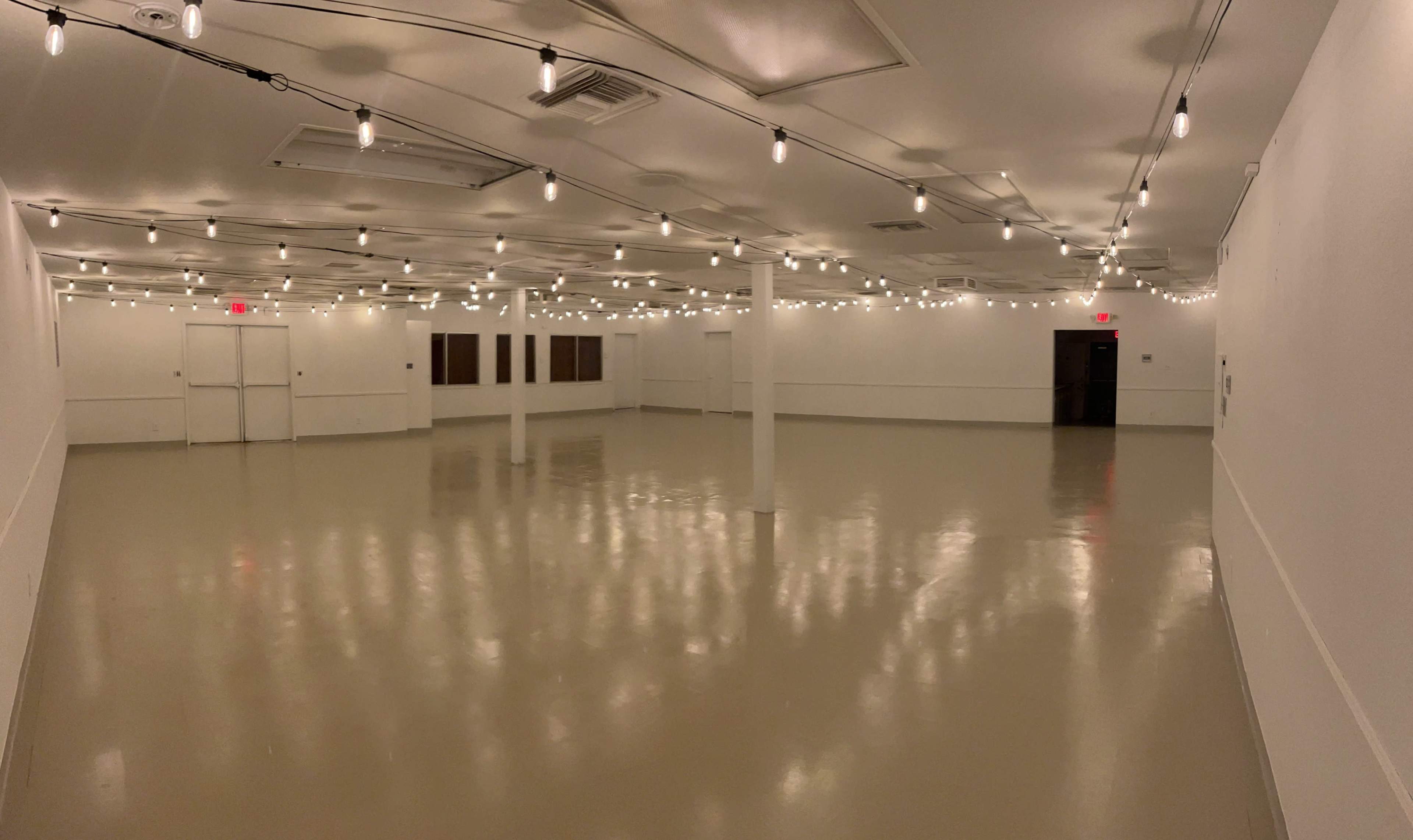 A spacious, brightly lit room with polished floors and decorative string lights hanging from the ceiling.