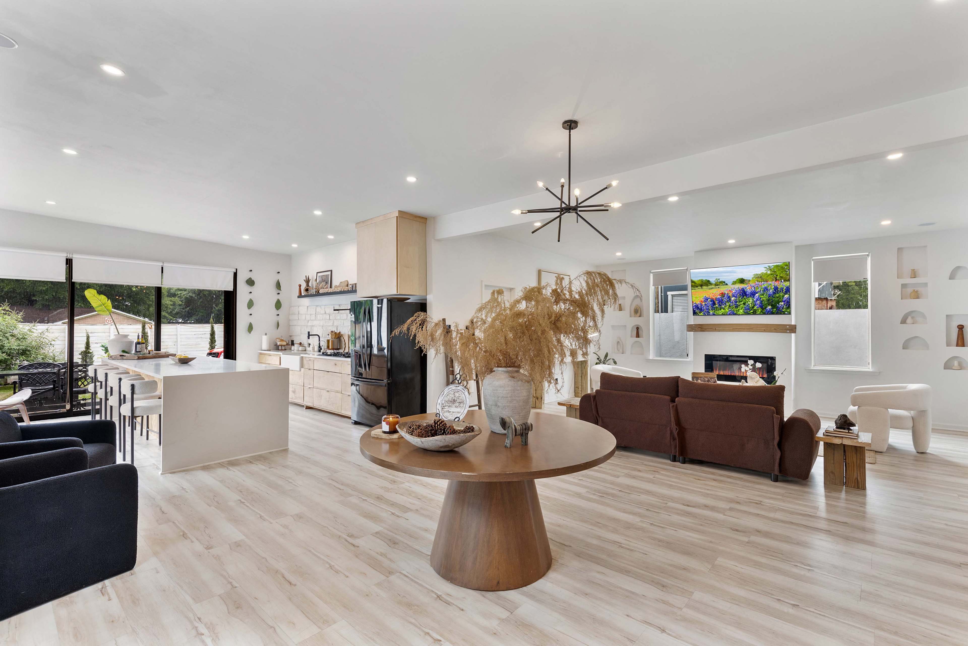 A spacious, modern living area features a round dining table, a kitchen with sleek cabinetry, and a seating area centered around a fireplace.
