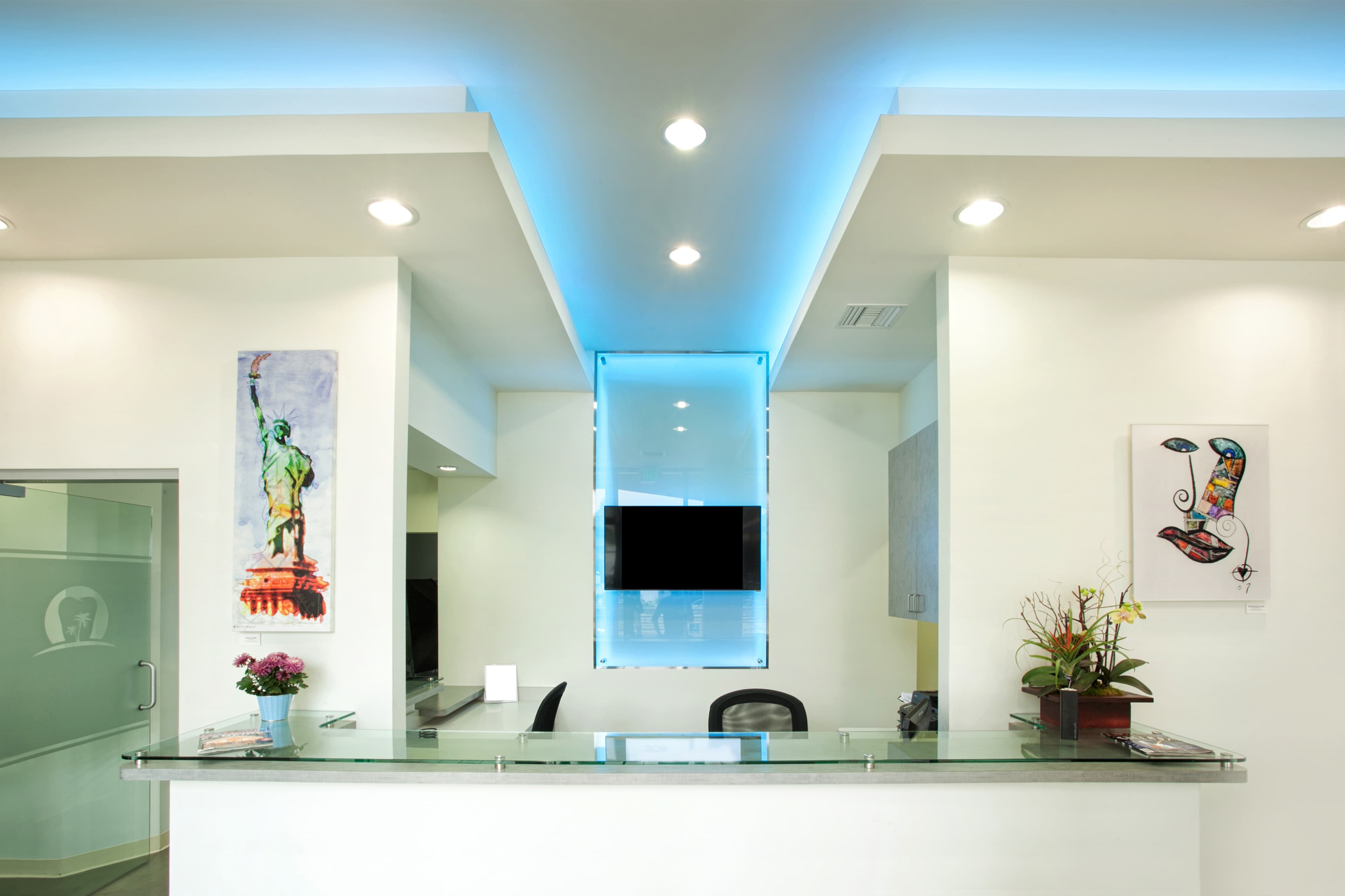 A brightly lit reception area features a glass countertop, modern decor, and artwork on the walls.