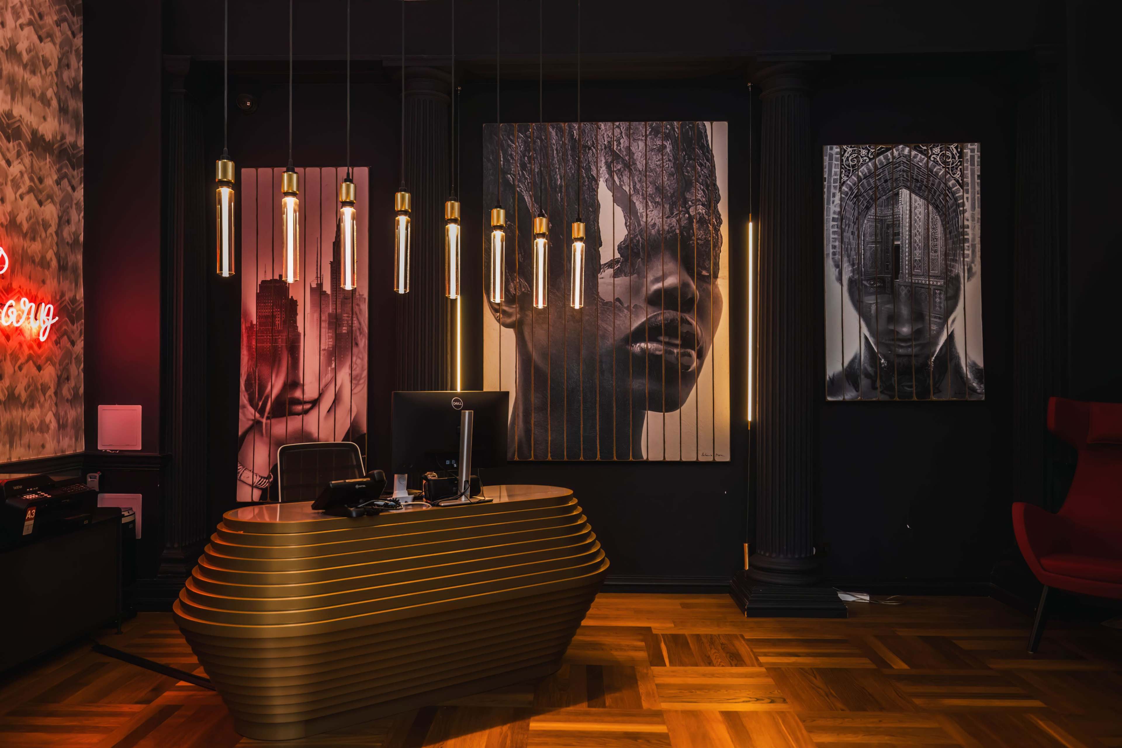 The image shows a modern reception area featuring a sleek golden desk, hanging light fixtures, and large black-and-white portraits on the walls.