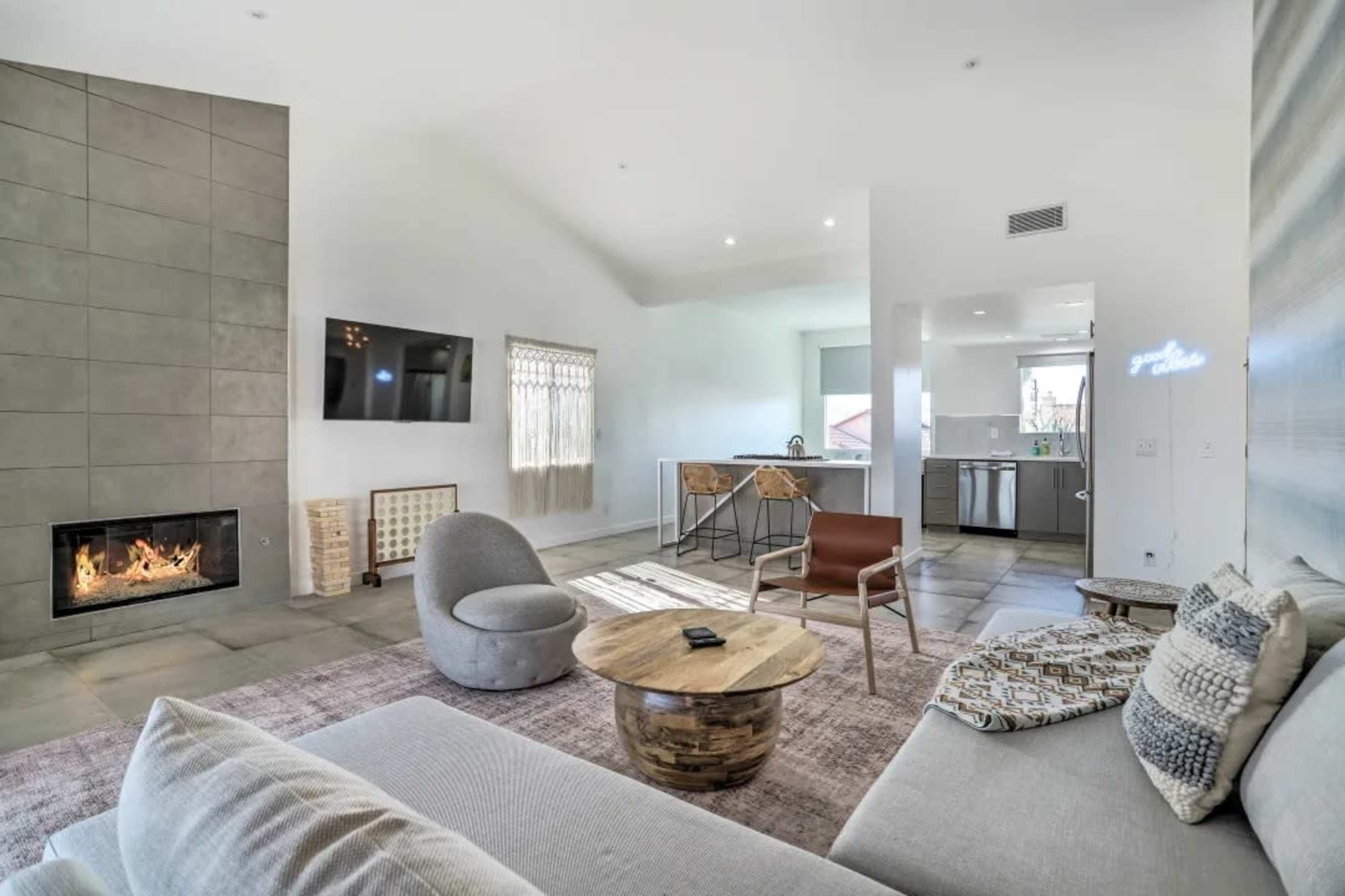The image shows a modern living room with a fireplace, a large sofa, and a view into an adjoining kitchen area.