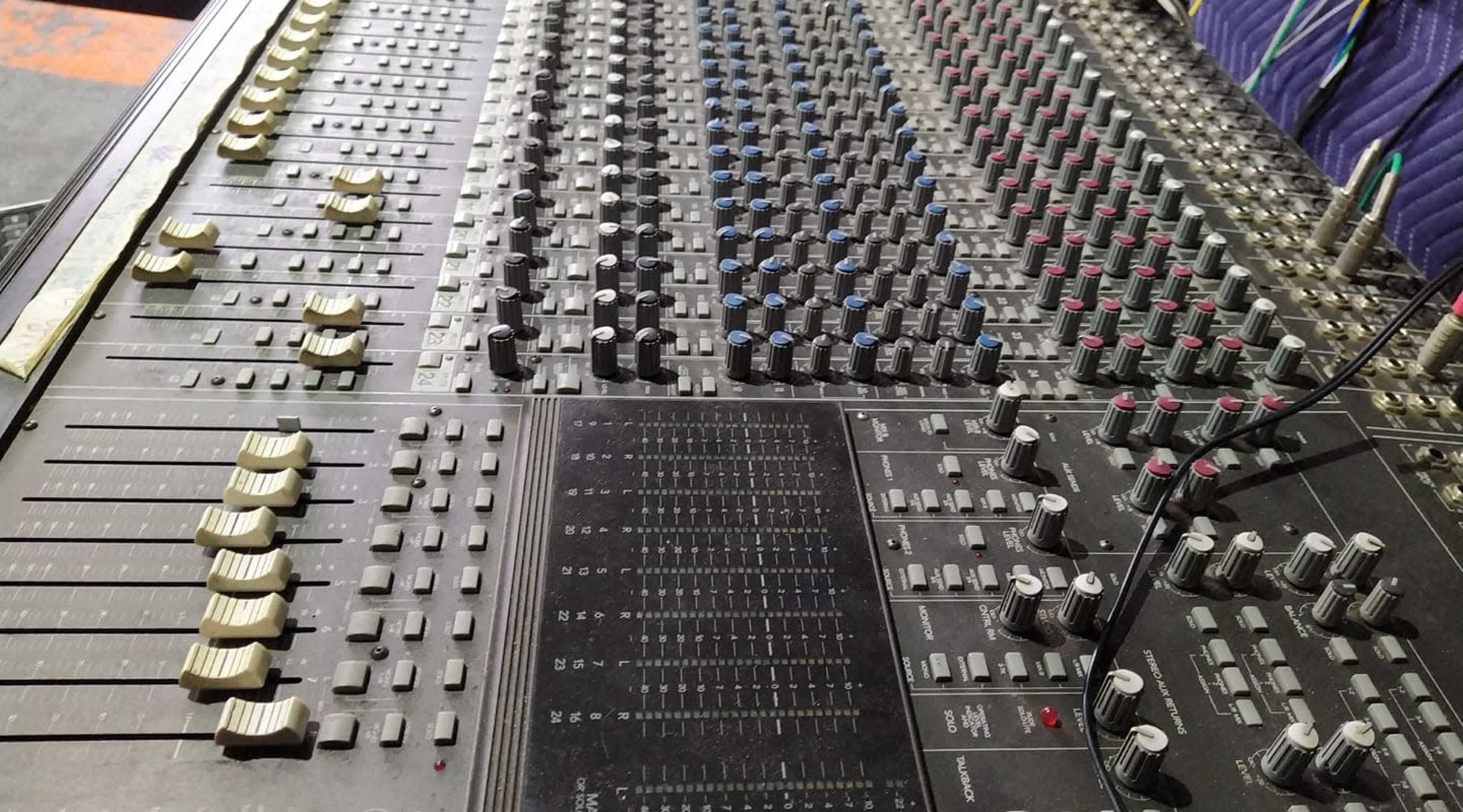 A close-up view of a large audio mixing console with numerous knobs, faders, and buttons.