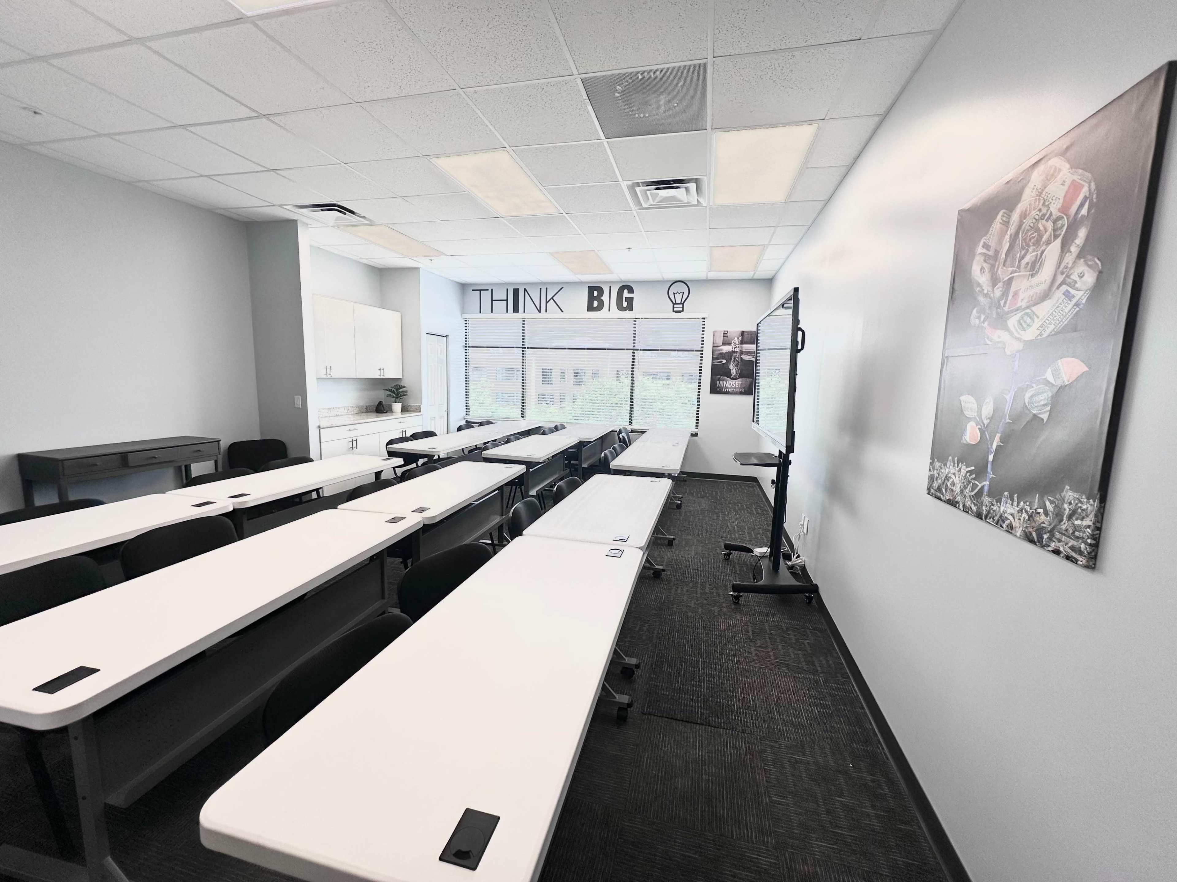 A modern classroom features rows of white tables and chairs, with a large screen and motivational wall art that says "THINK BIG."