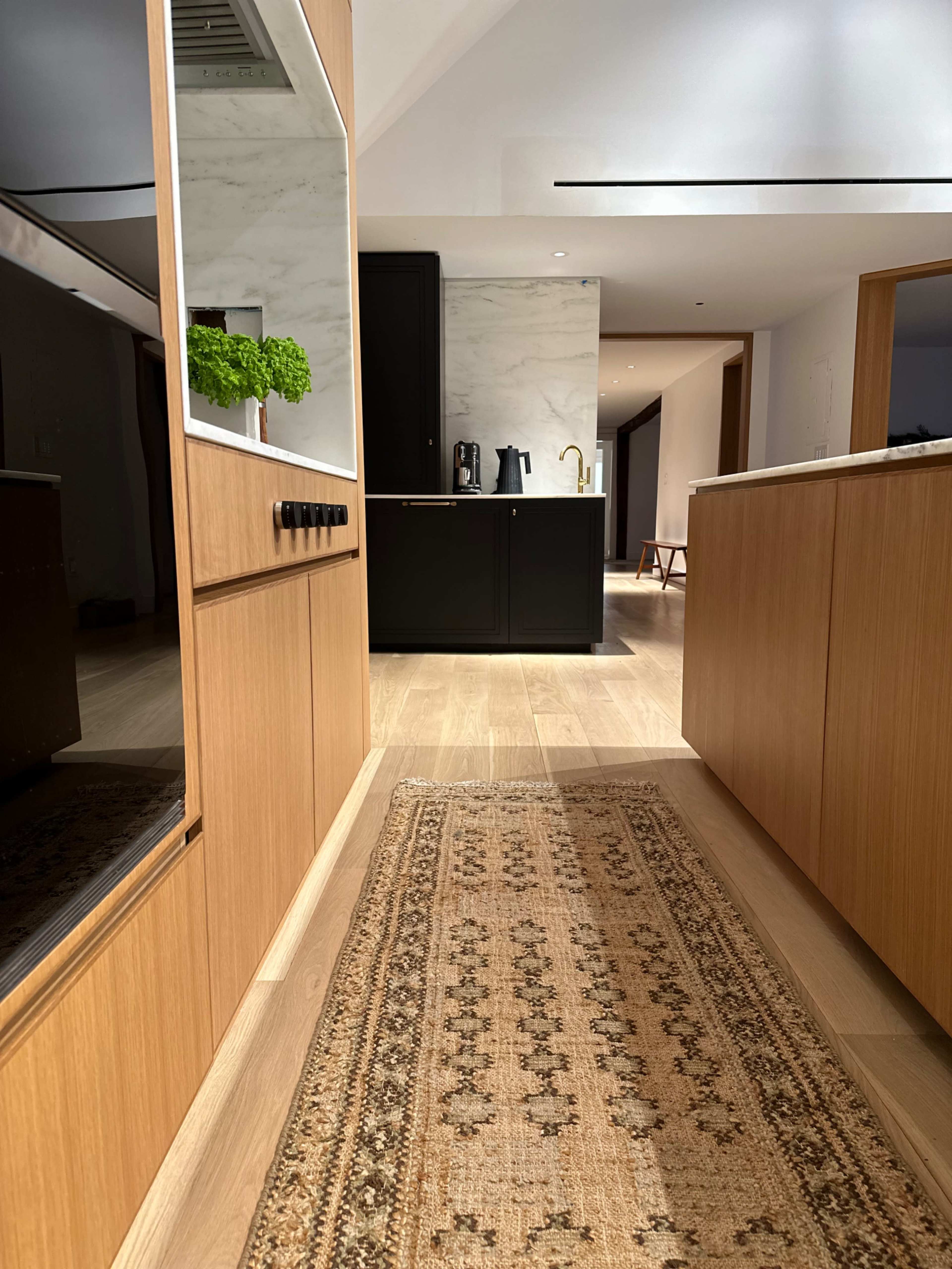 A modern kitchen with wooden cabinetry and a long, patterned runner rug along a wooden floor.