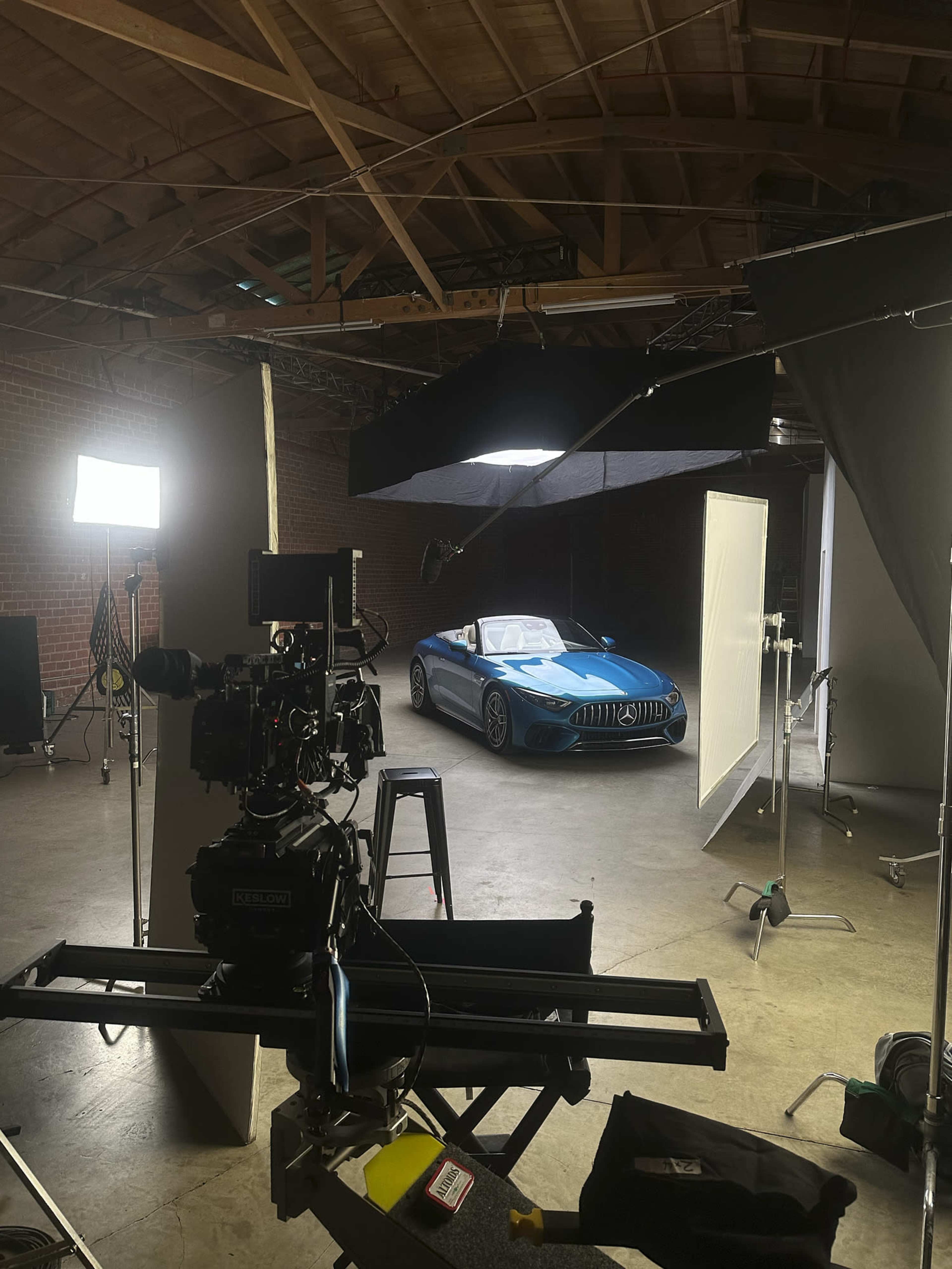 A camera setup is positioned in a studio, focusing on a blue sports car parked under studio lights.