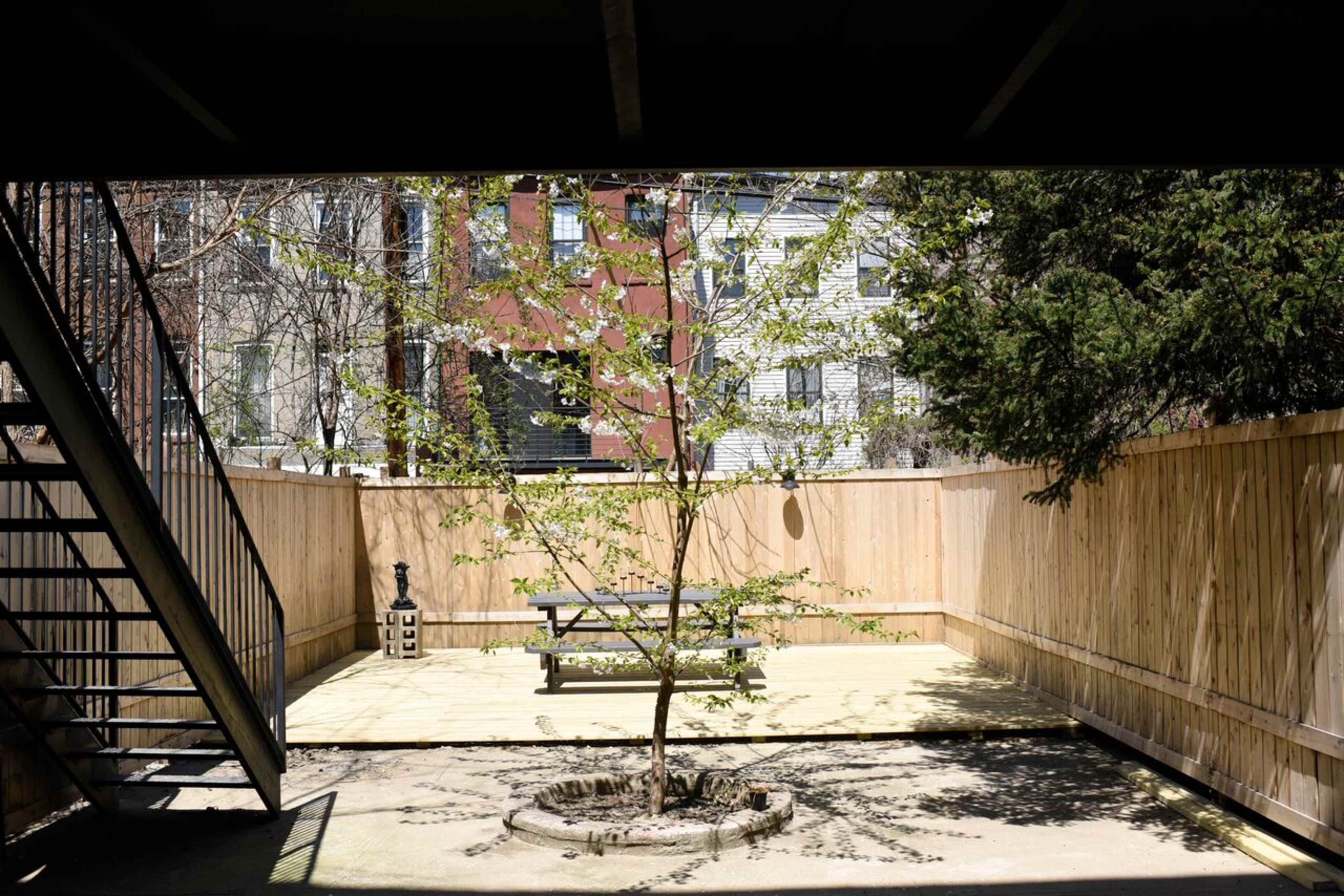 A small courtyard features a central tree surrounded by wooden fencing and a picnic table on a light-colored platform.
