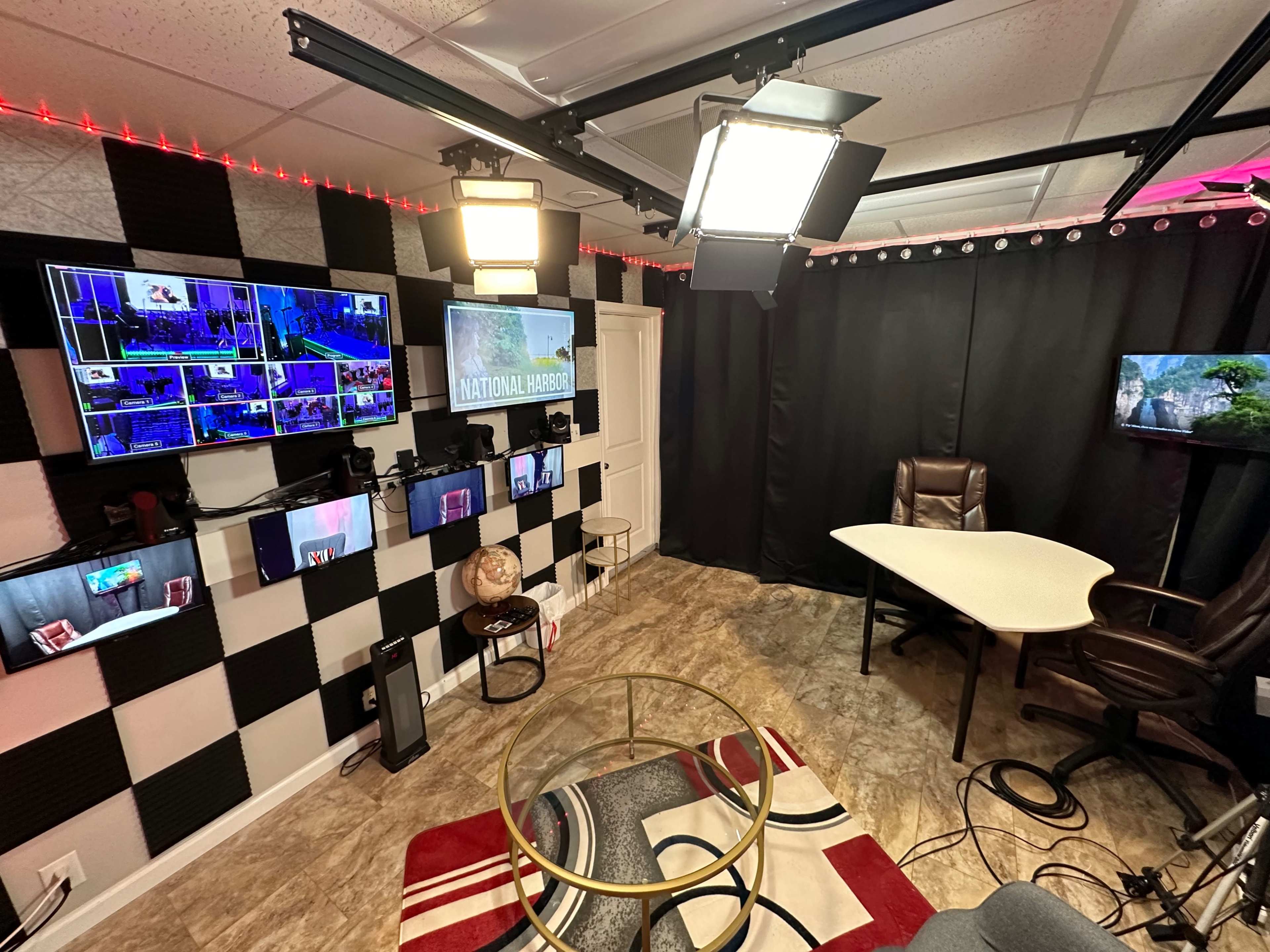 A small studio or office space equipped with multiple screens, a desk, and a comfortable chair, all surrounded by patterned walls and lighting.