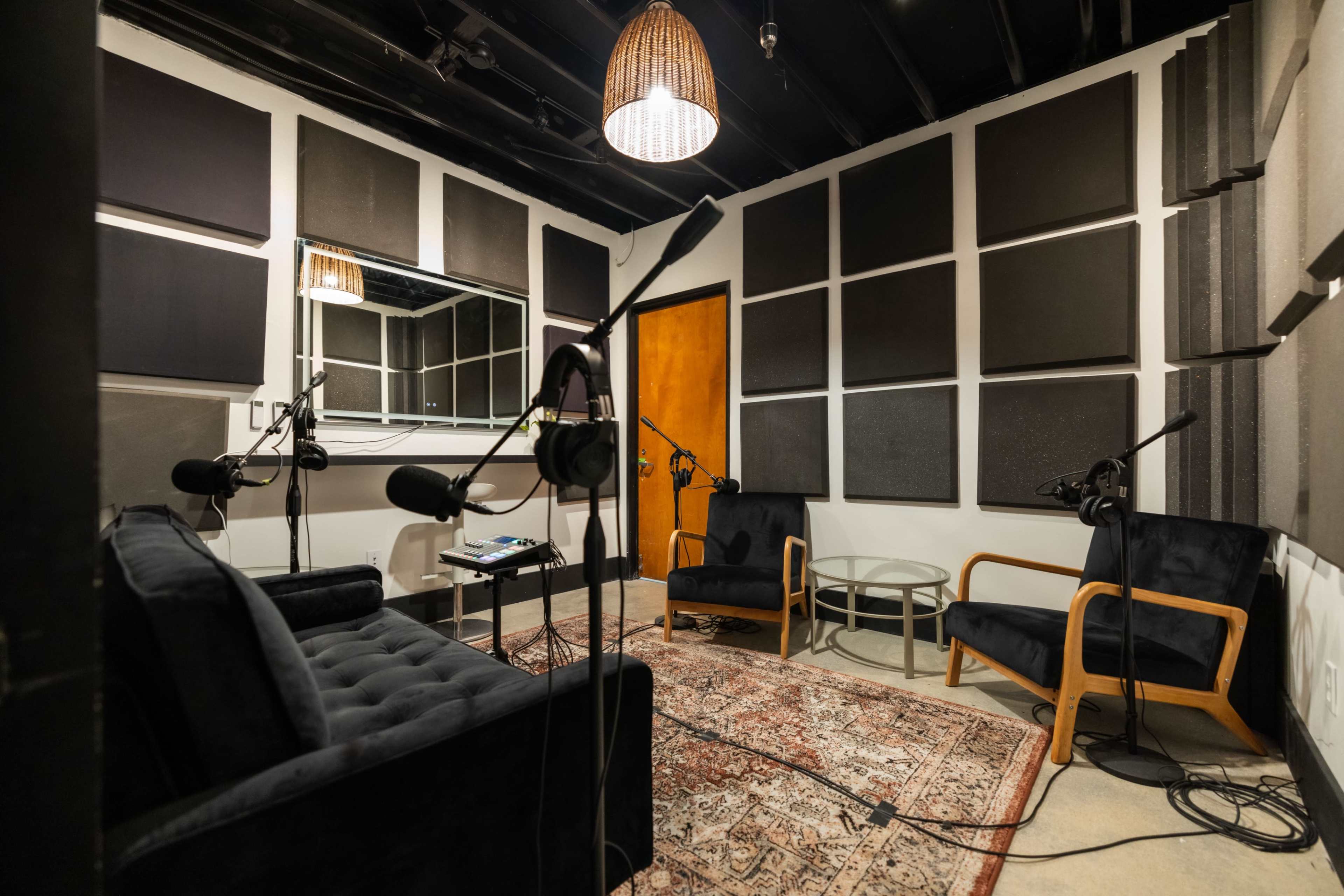 A small recording studio with soundproofed walls, two chairs, a table, and several microphones positioned around the room.