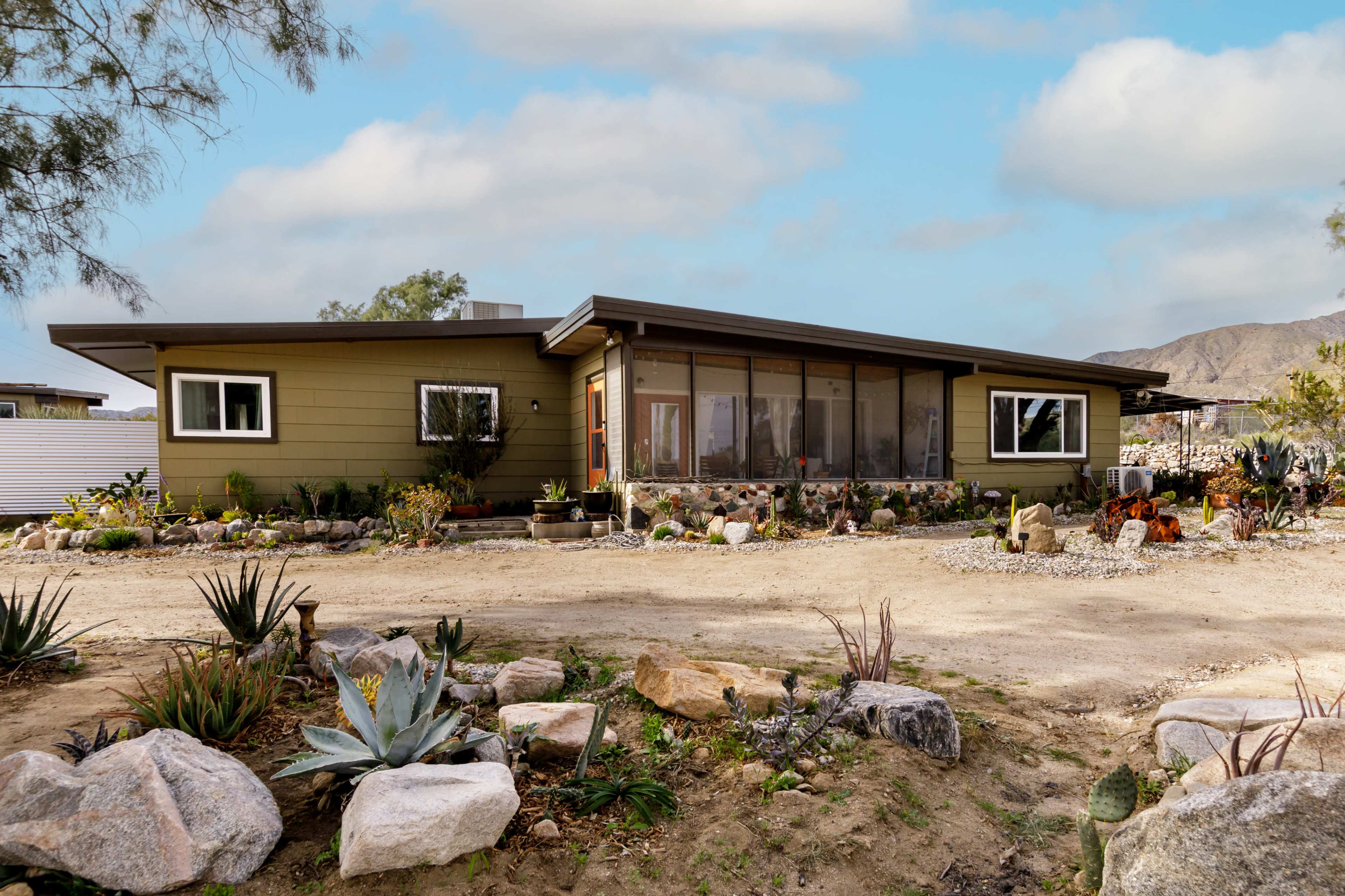 A single-story home with a screened porch and desert landscaping sits at the end of a gravel driveway.