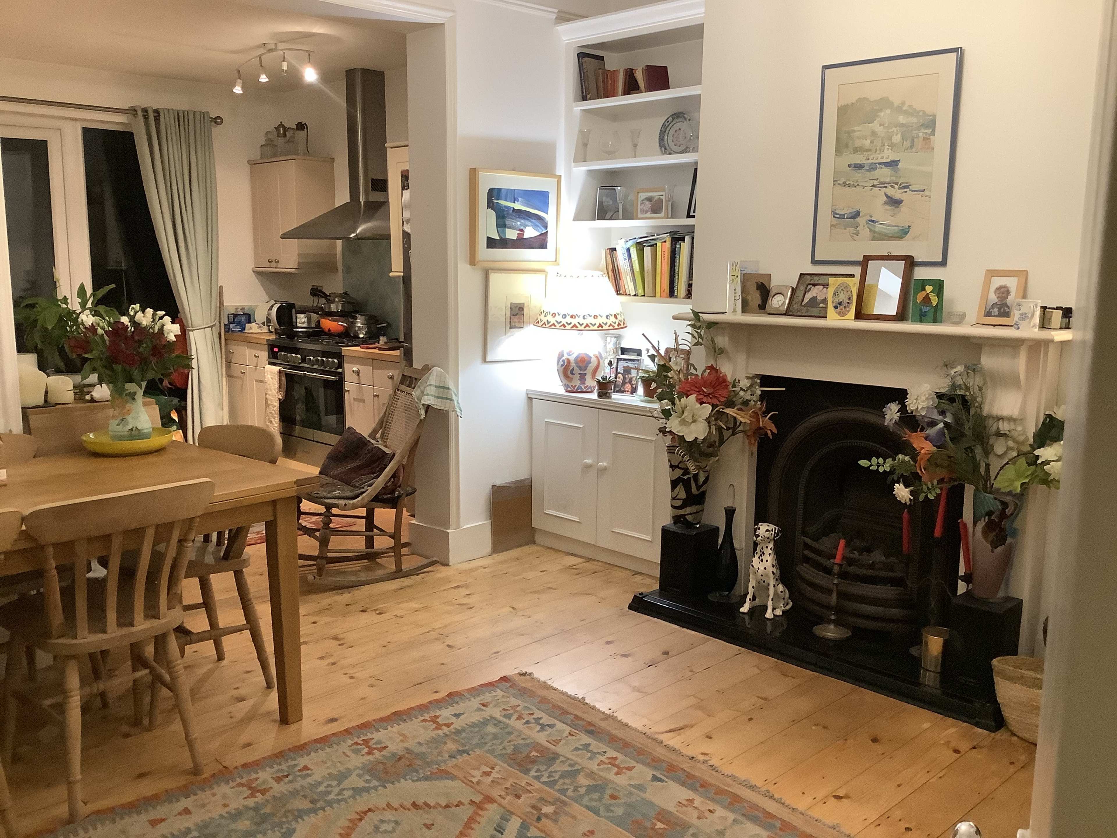 A cozy kitchen and dining area featuring a wooden table, a fireplace adorned with plants and decor, and a view of the cooking space.