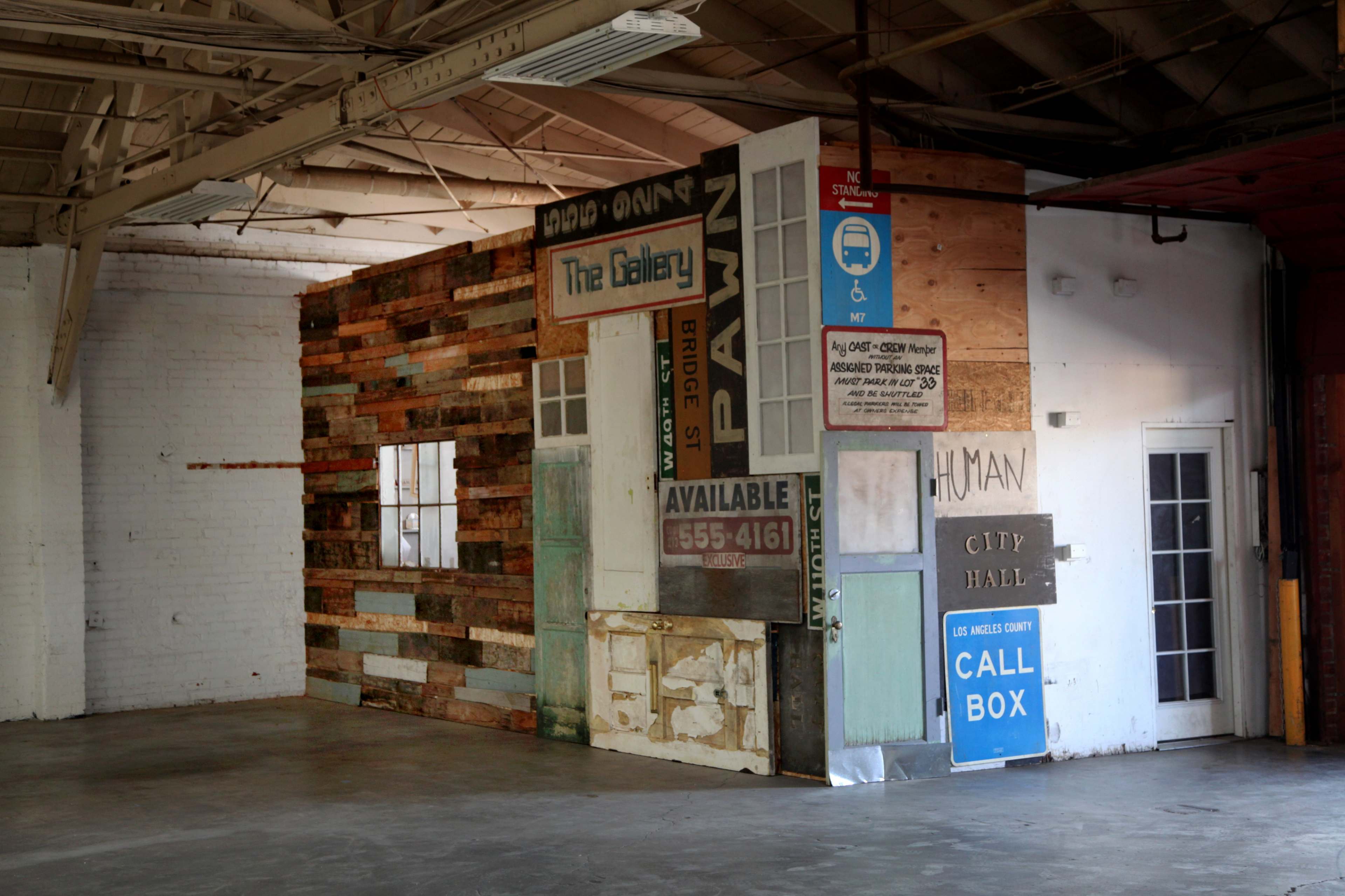 The image shows a large, open industrial space featuring a wall made from an assortment of wooden planks and old signs.