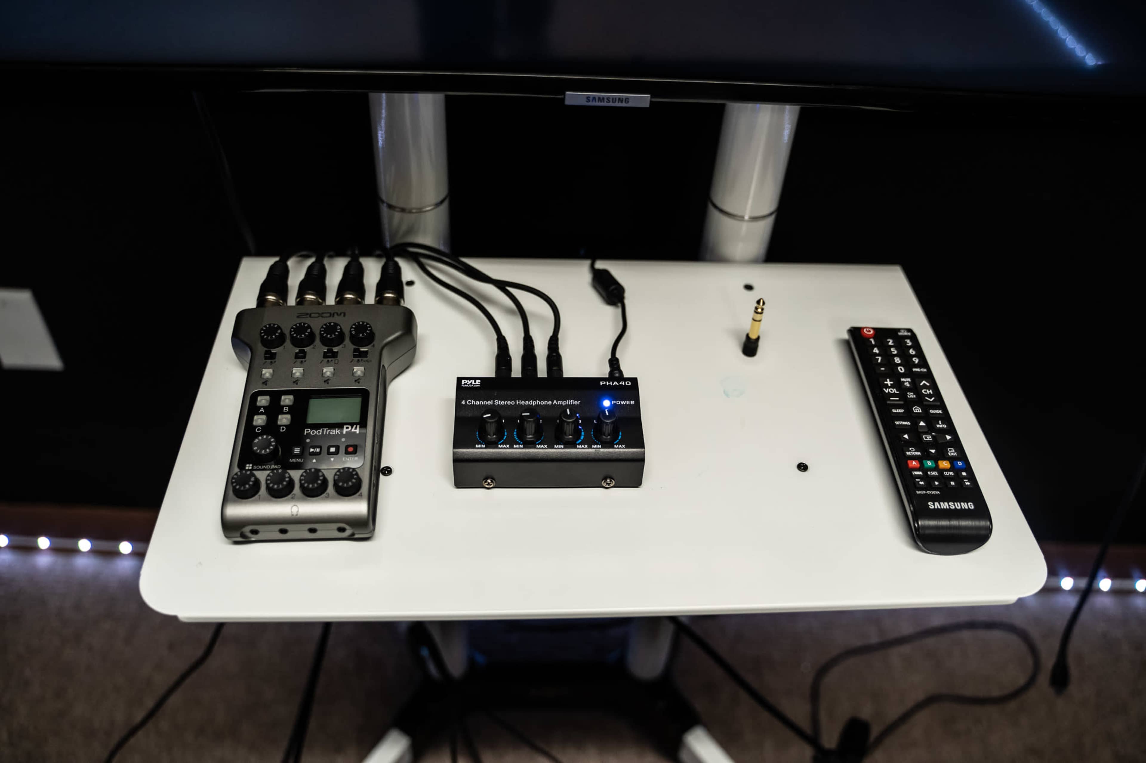 A white table features an audio mixer, a multi-channel mixer, and a remote control, all connected by various cables.