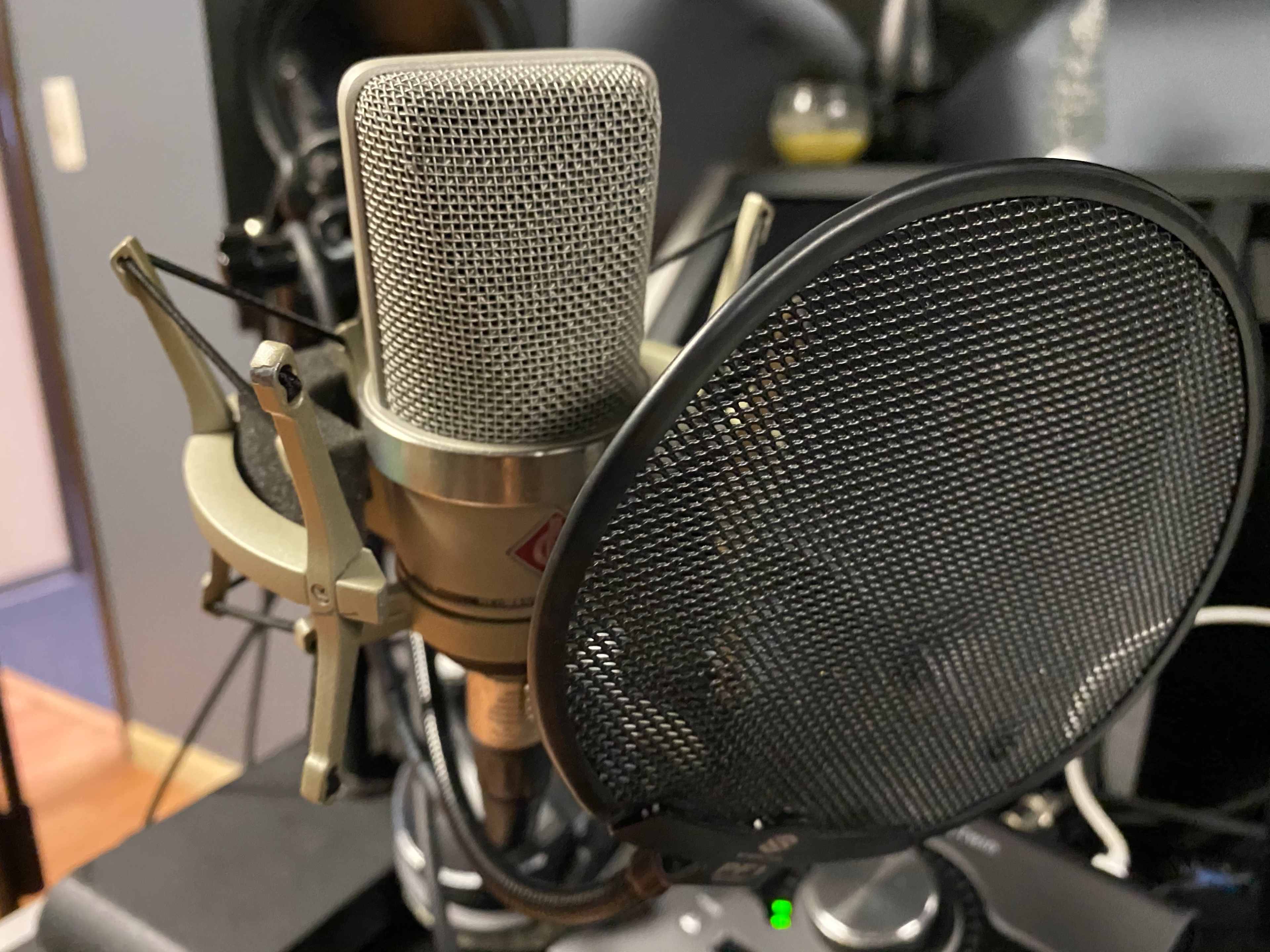 A microphone with a pop filter is positioned on a desk in a recording studio.