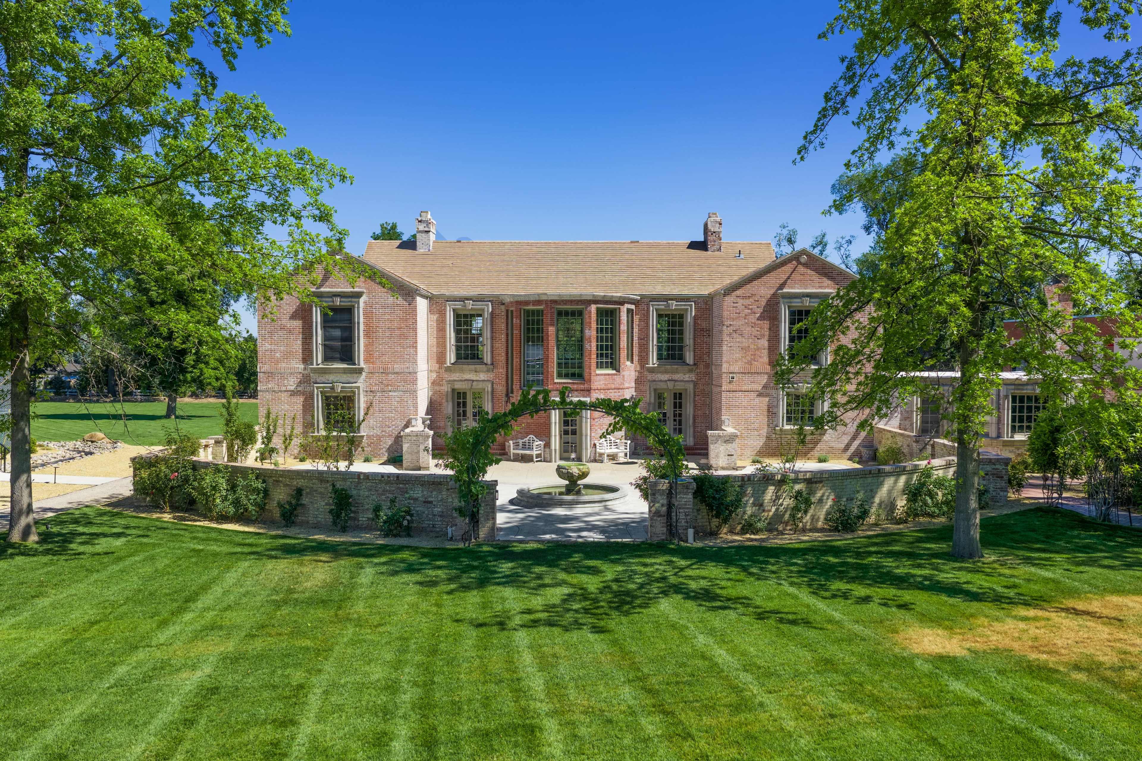 The image shows a large brick house with a manicured lawn and trees framing the exterior.