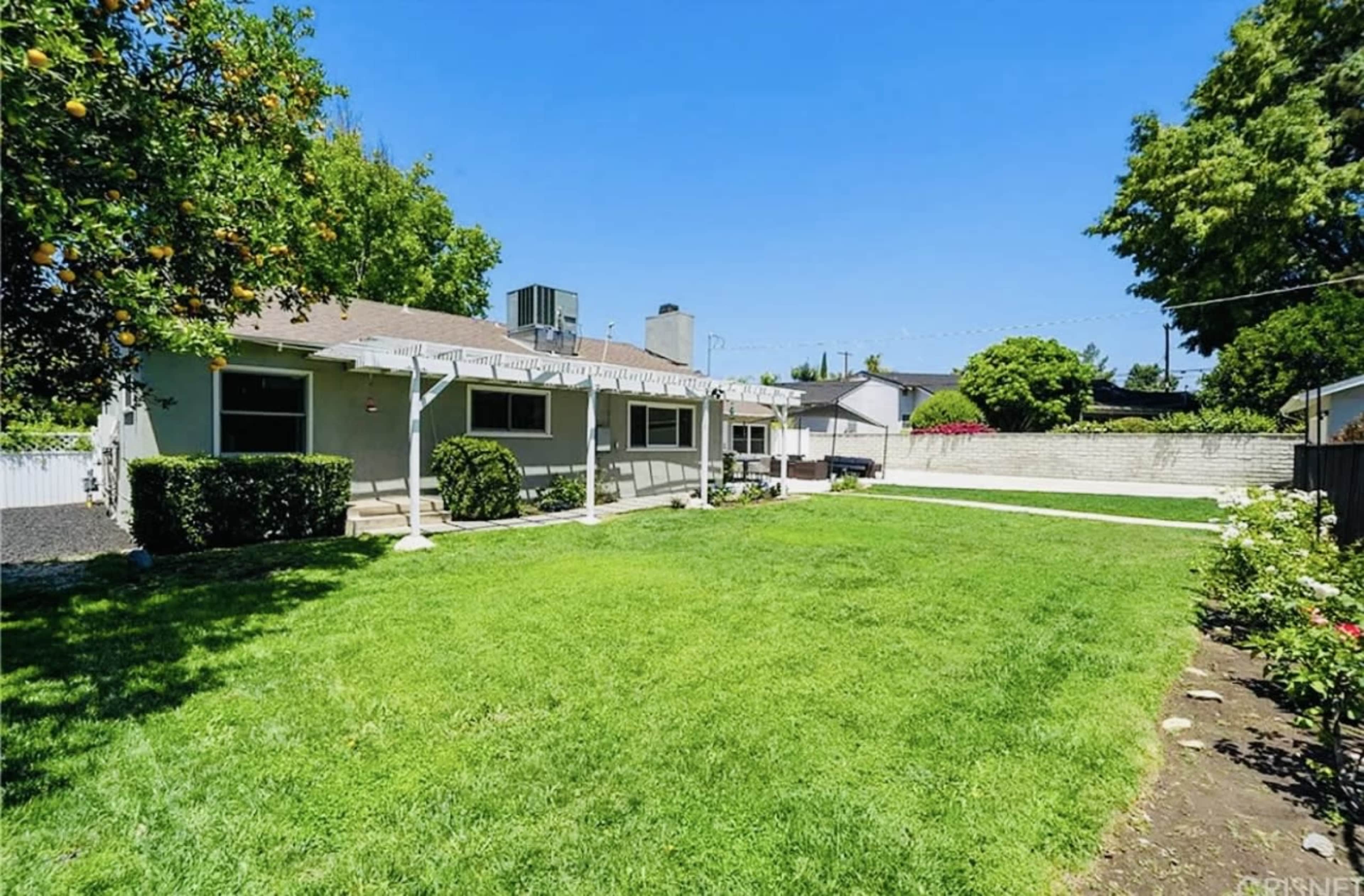 A backyard with a well-maintained lawn, a house with a patio, and surrounding trees.