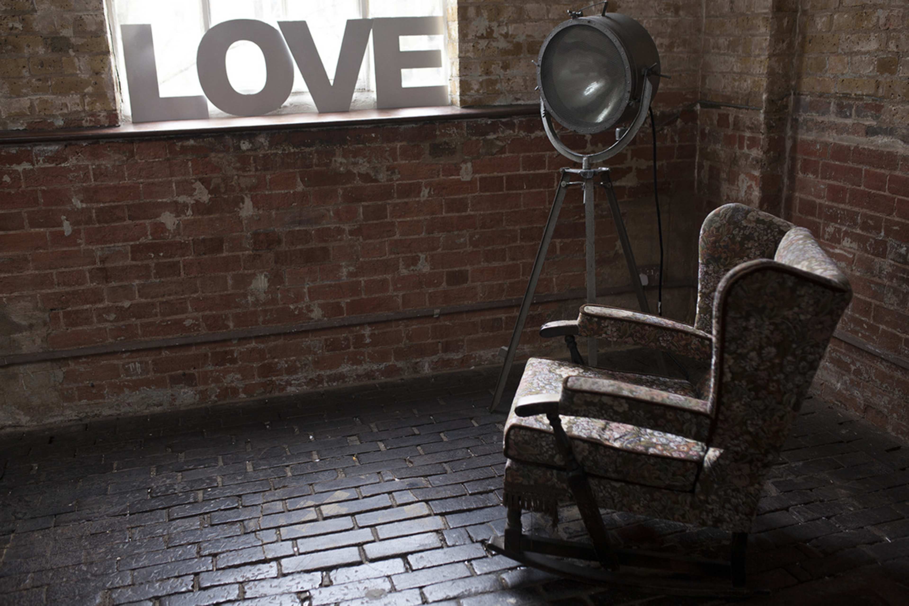 Two vintage floral armchairs beside a large, industrial light and the word "LOVE" displayed in capital letters on a brick wall.