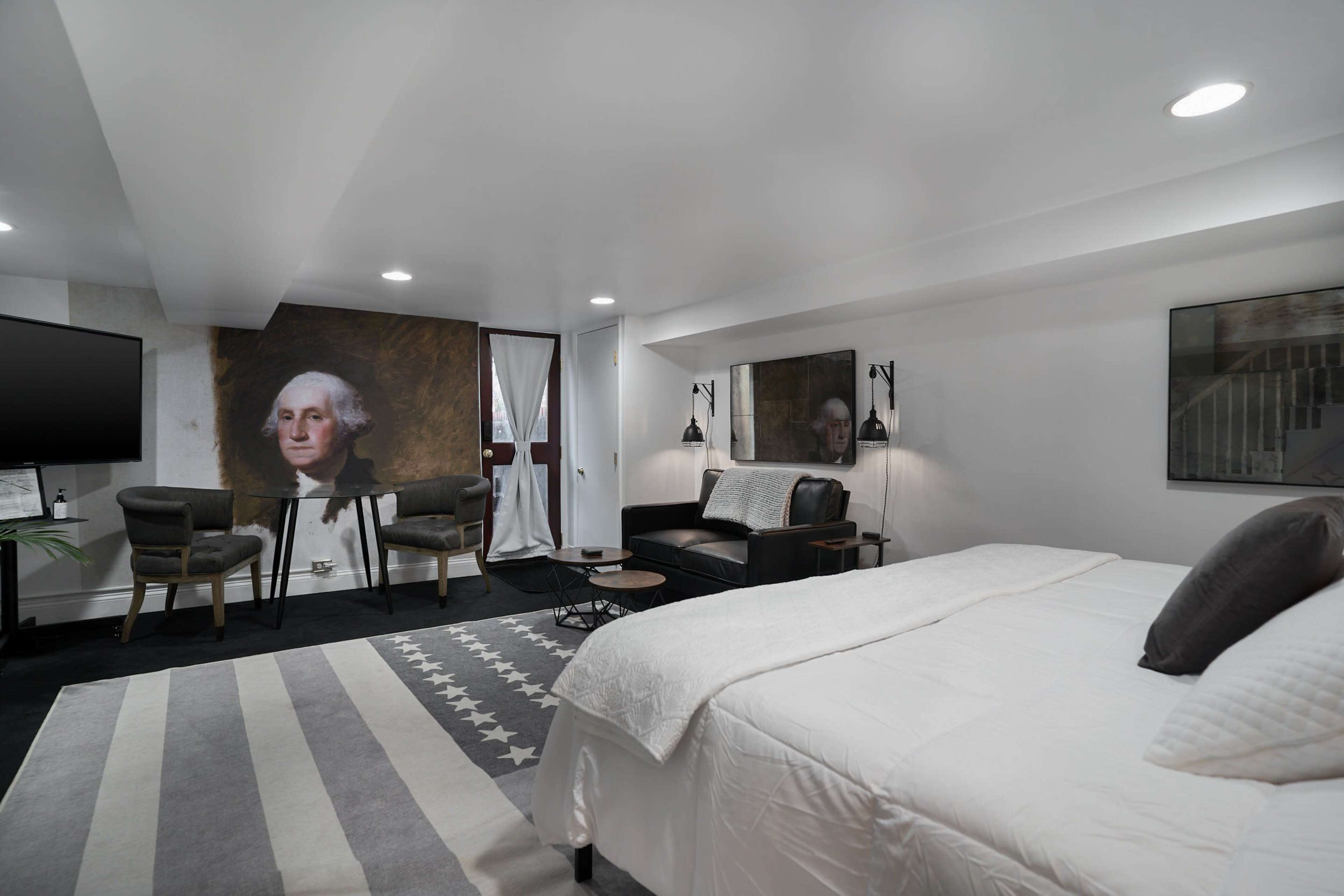 The image shows a modern room with a bed, seating area, and a large portrait of George Washington on the wall.