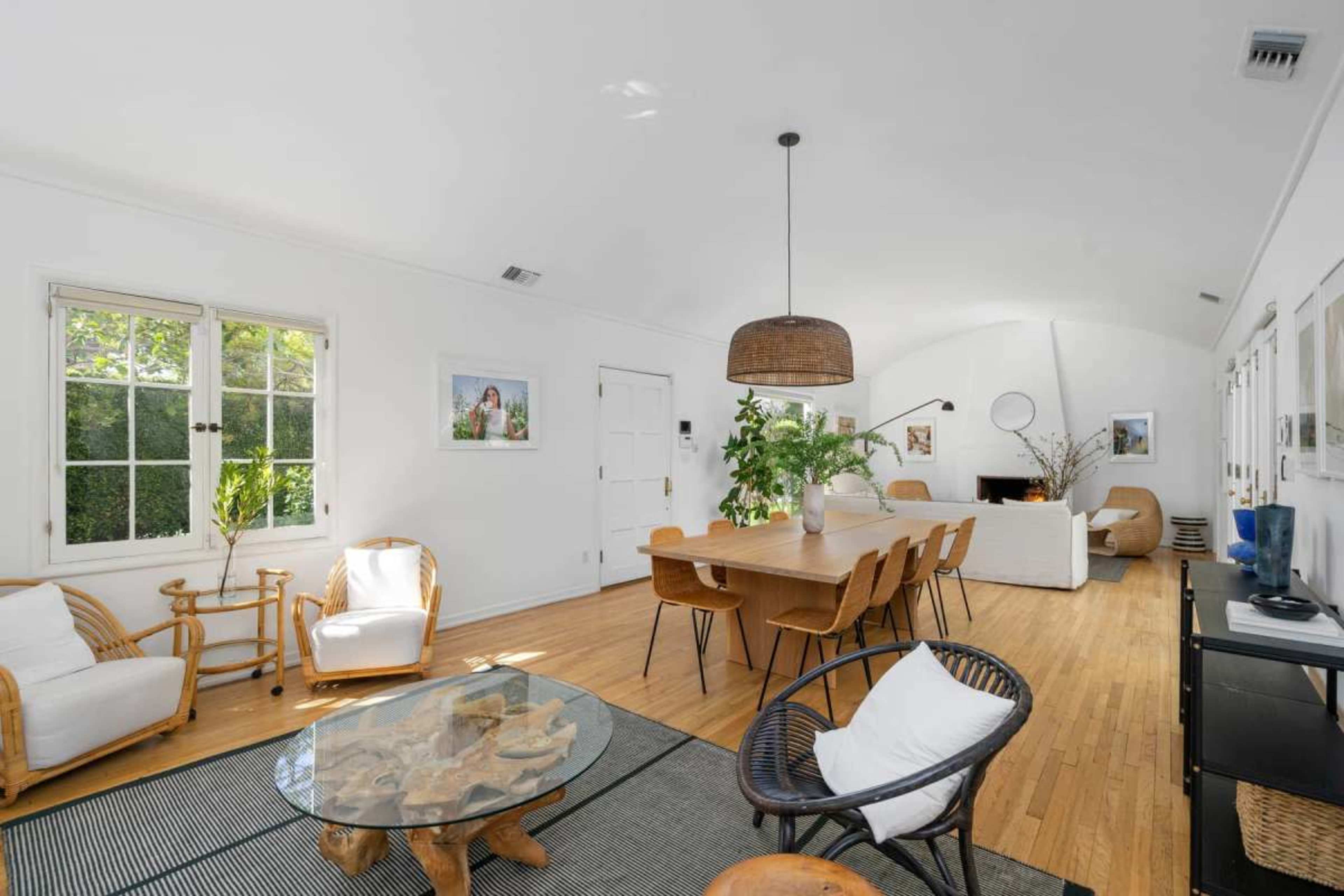 The image shows a bright, open-concept living and dining area with wooden flooring, a long dining table, and various seating arrangements.