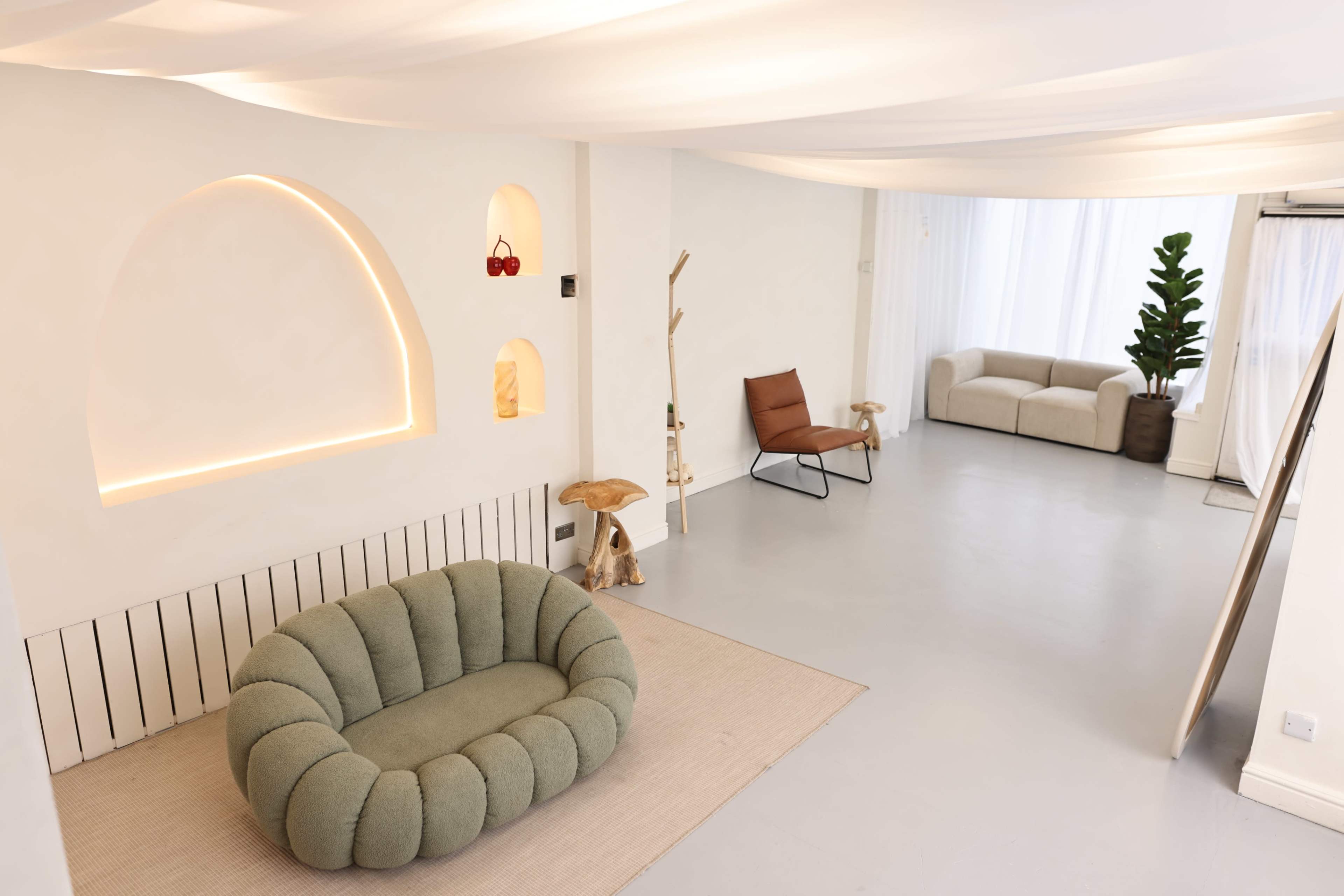 The image shows a modern, minimalist living space with a green, plush sofa, a tan armchair, and decorative shelves set against white walls.